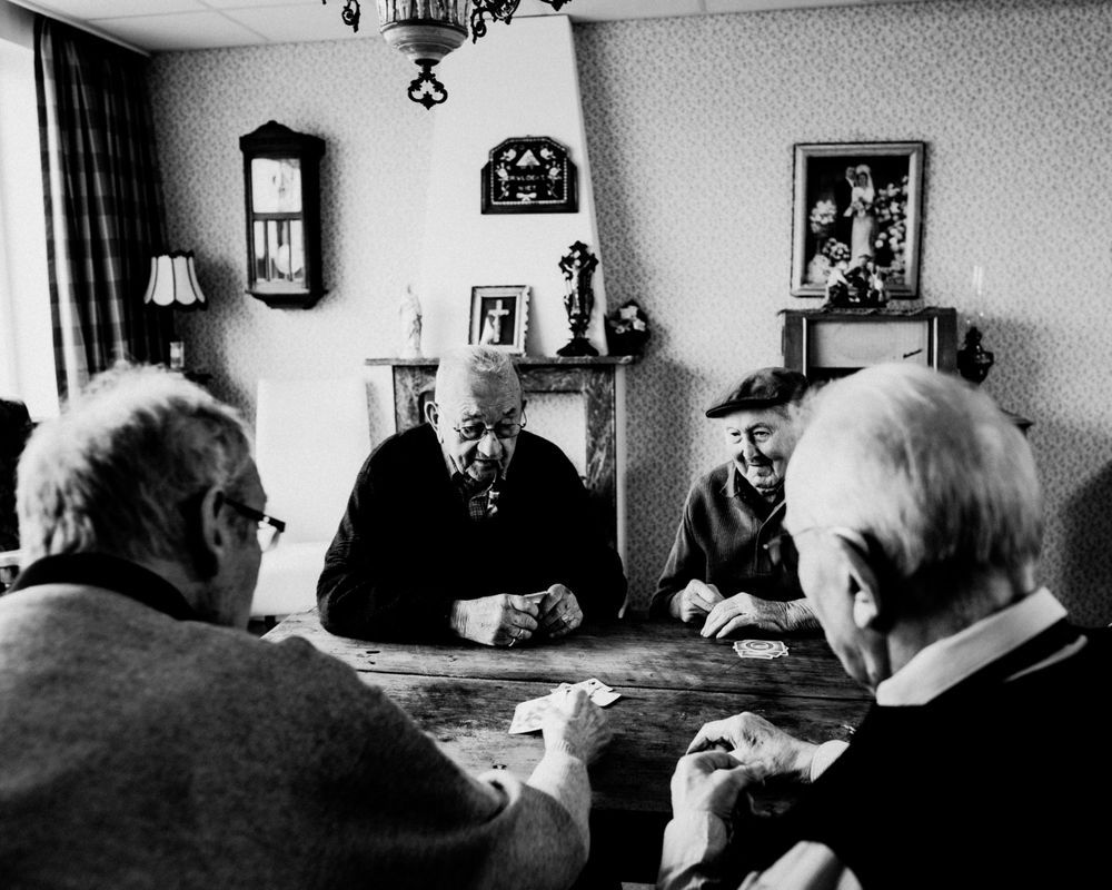 Black and white photos show elderly people gathered in a room with furniture and wall decorations.