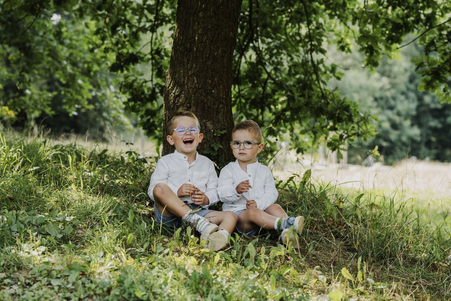 Candid family moments captured in a sunlit meadow with trees in the background.