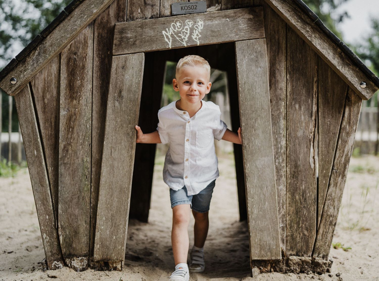 Child exploring a rustic wooden playhouse structure in a natural outdoor setting.