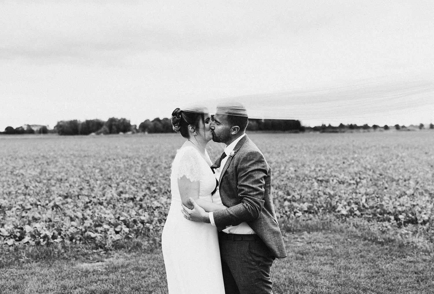 Black and white photo of a couple kissing in a field on their wedding day, bride in white dress and groom in suit.