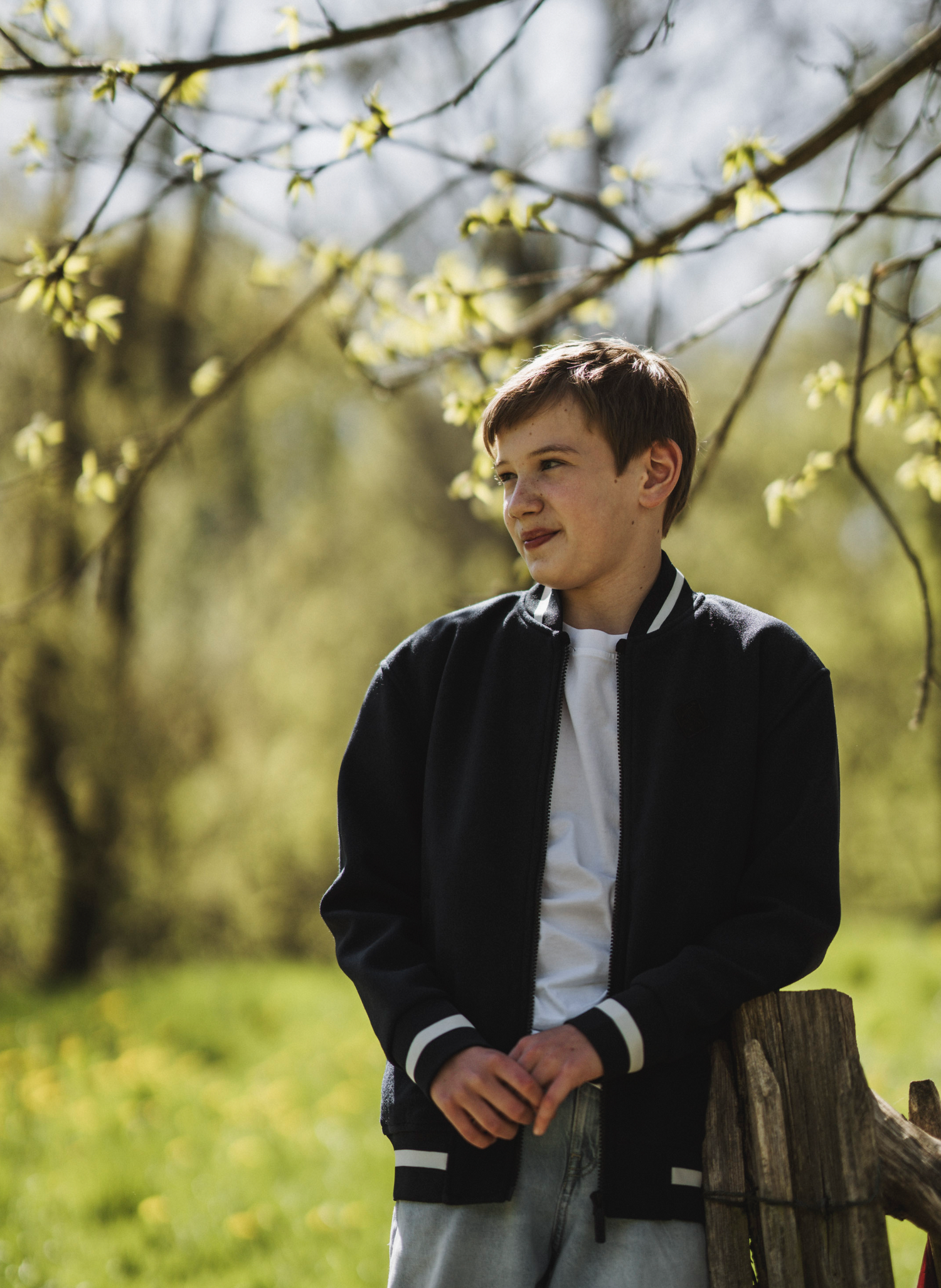 A spring portrait features someone in a dark jacket against blooming yellow branches.