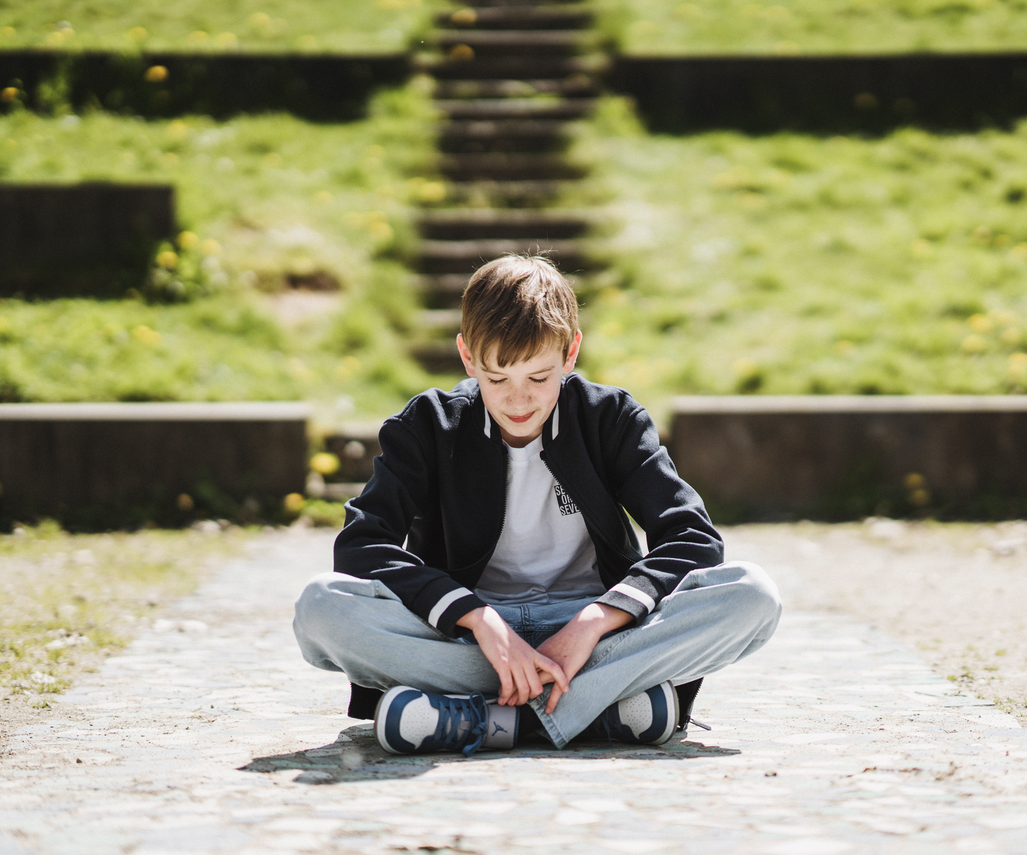 A casual outdoor portrait shows someone sitting cross-legged on concrete steps in a dark jacket.