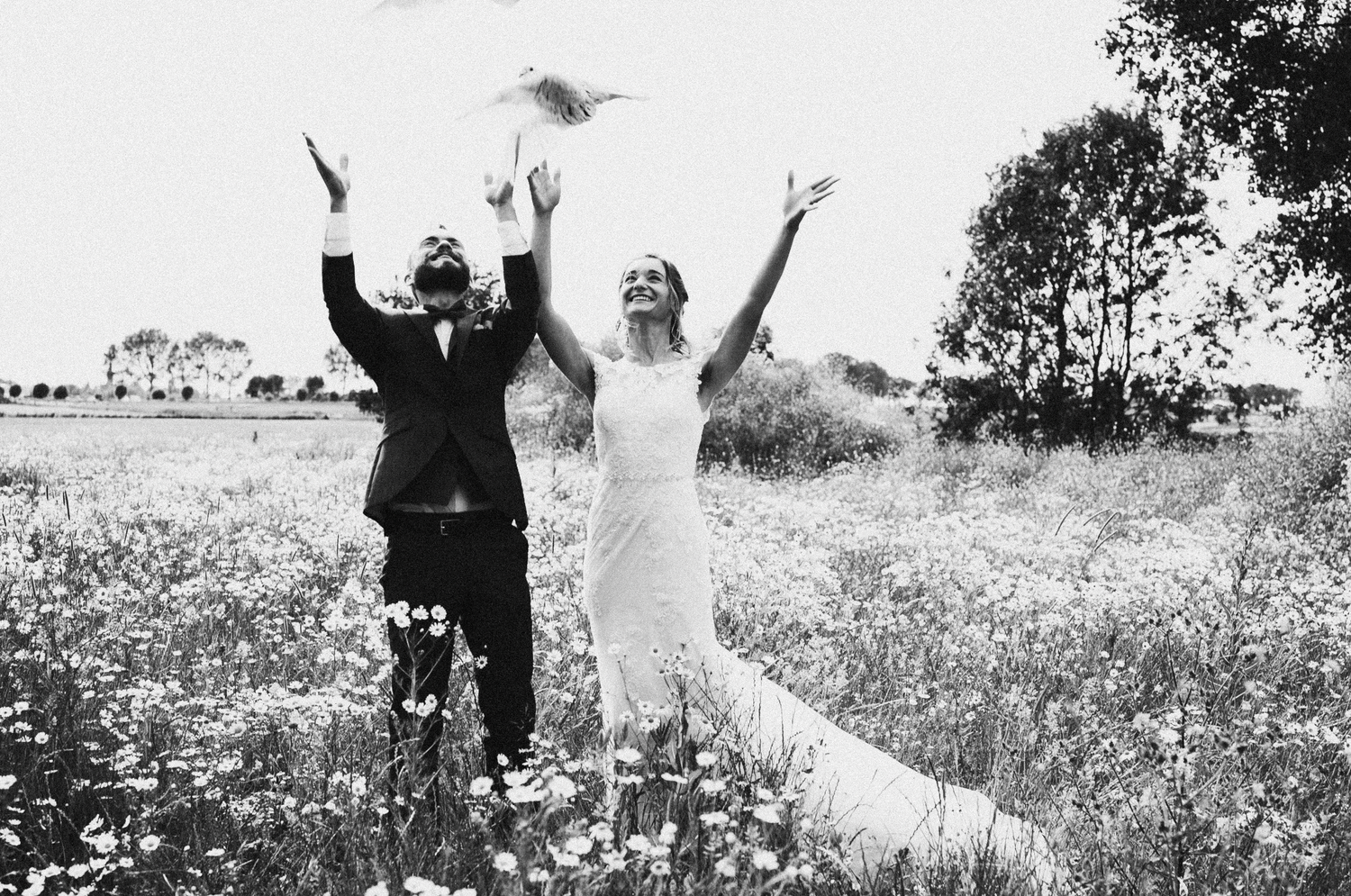 Black and white photo of a bride and groom releasing a dove in a wildflower field on their wedding day.