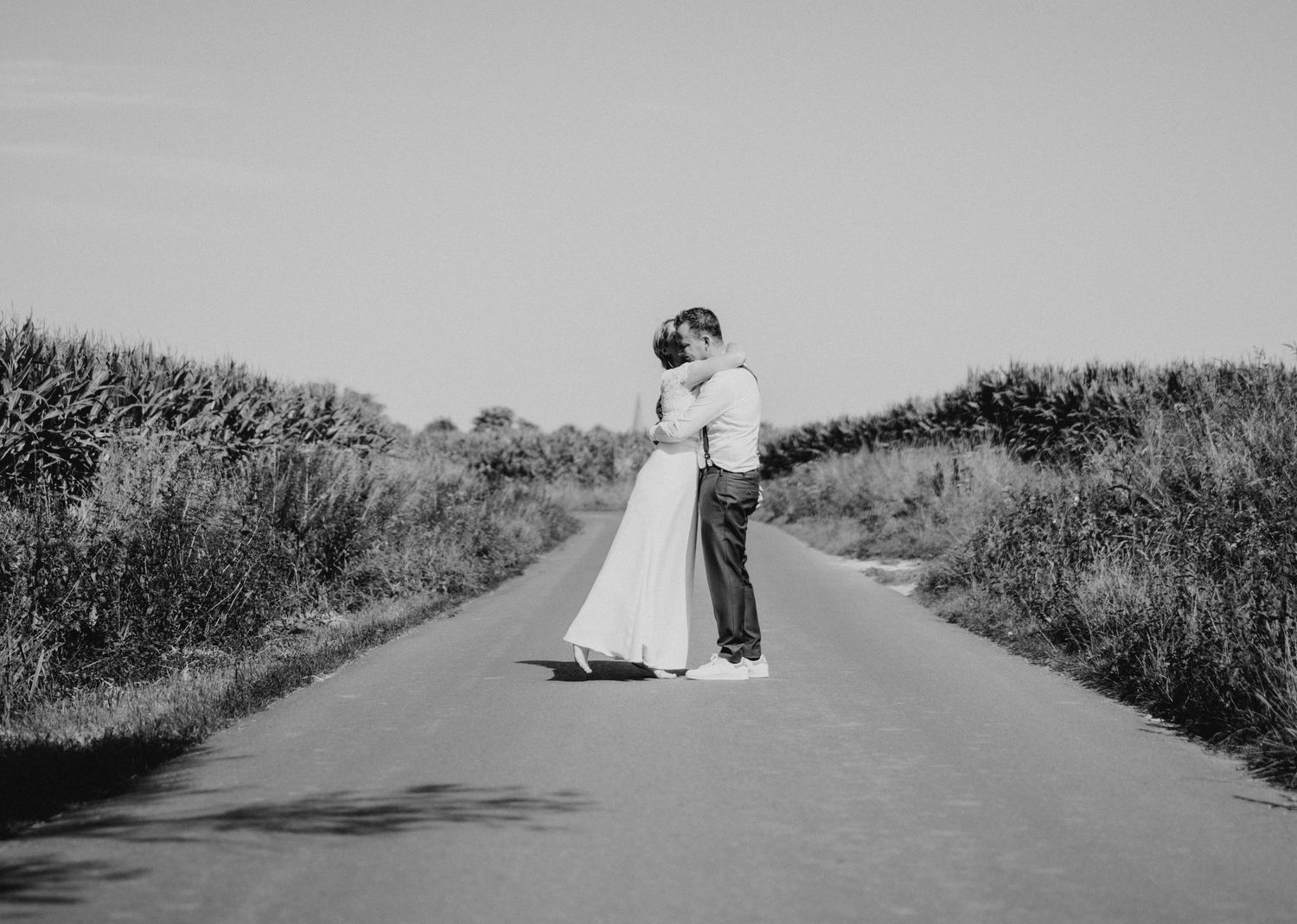 A black and white wedding portrait of a couple standing on an empty country road.