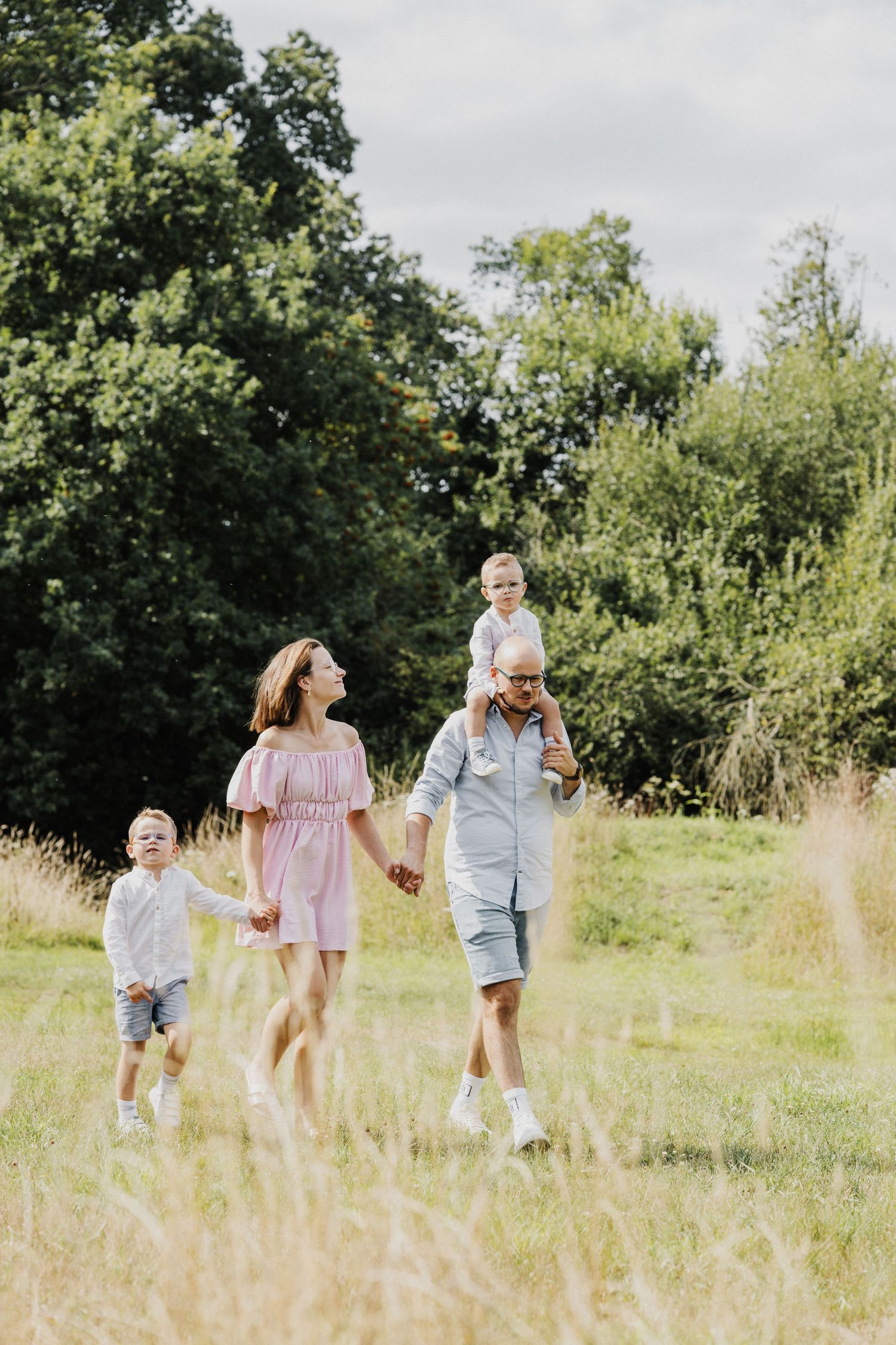 Family walking together through tall grass in a sun-drenched summer meadow.