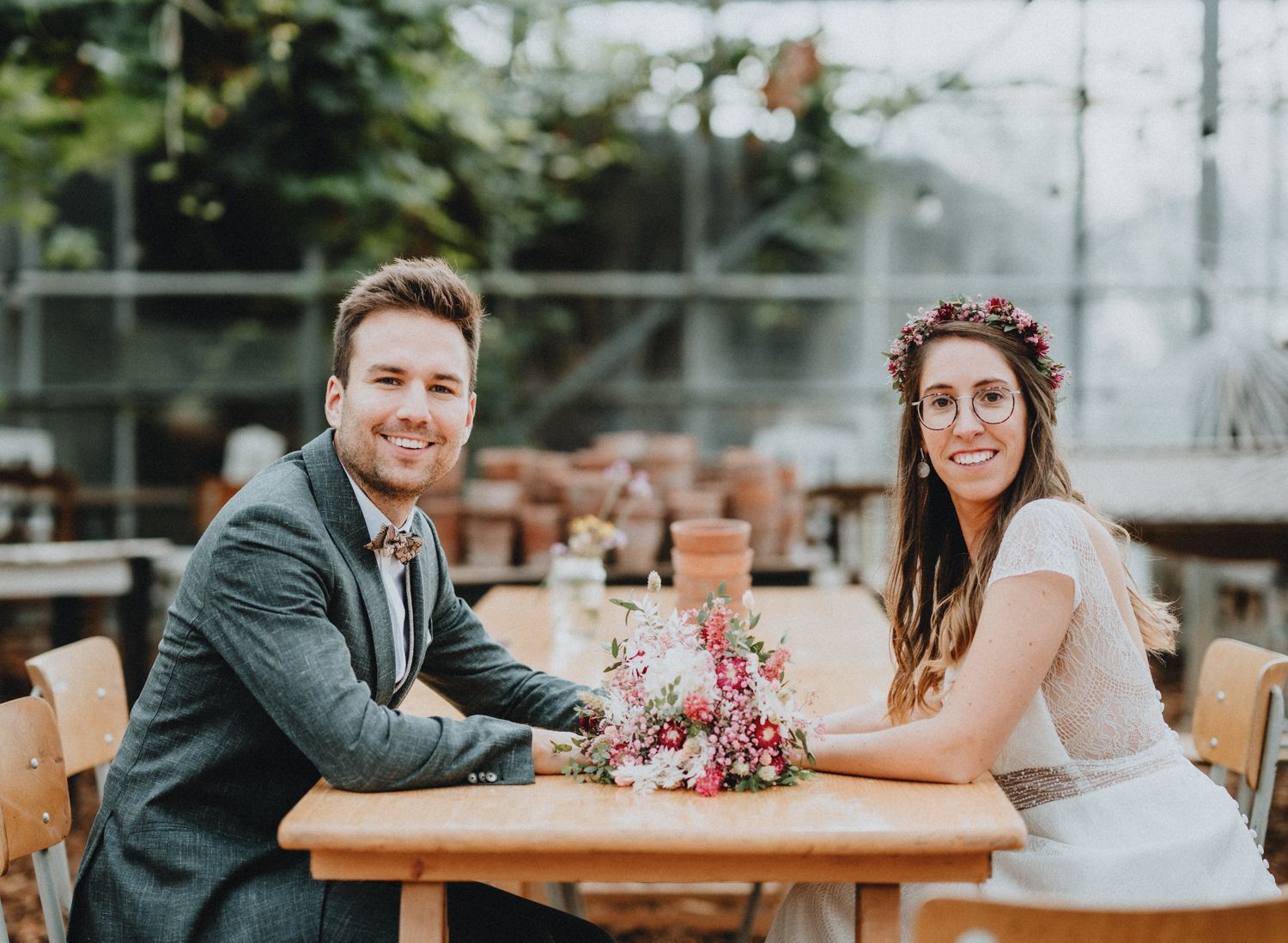 Wedding reception scene with rustic wooden tables and greenhouse backdrop.