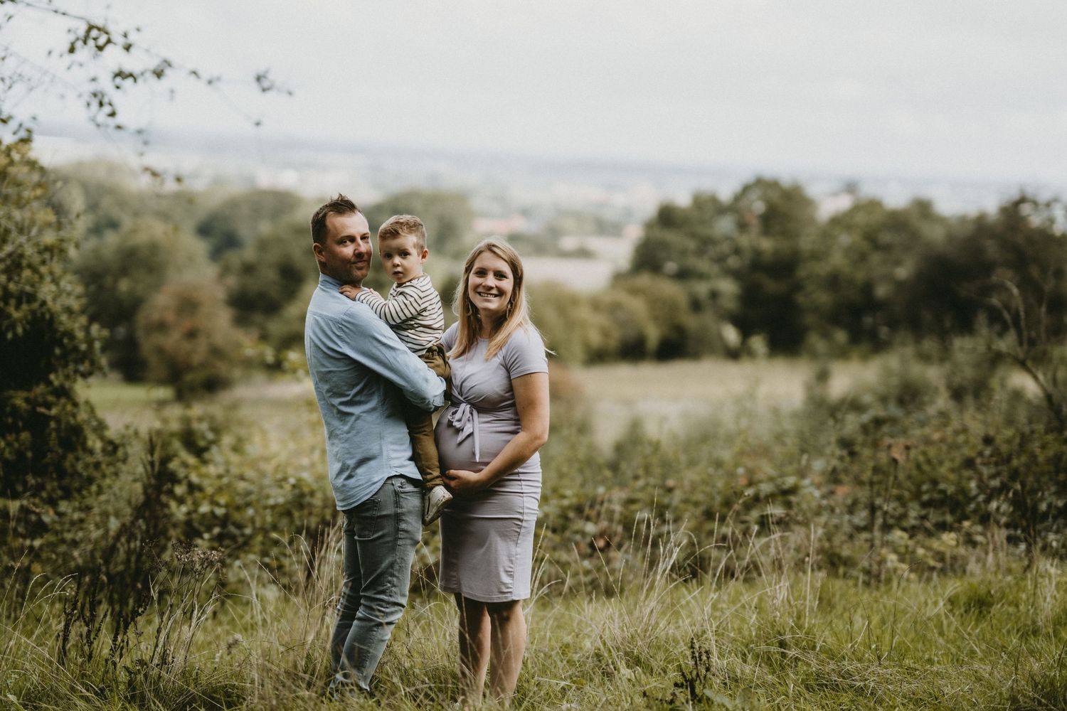 A family embraces while standing in a scenic grassy field during golden hour.