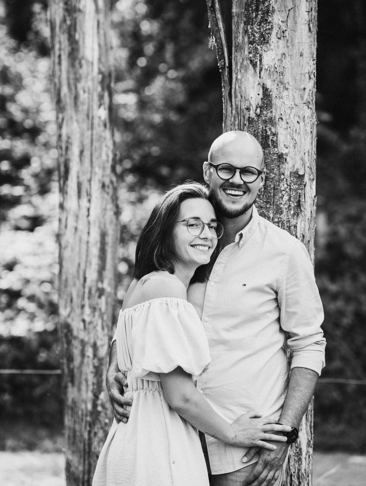 Black and white portraits of a couple embracing against tree trunks in a natural setting.