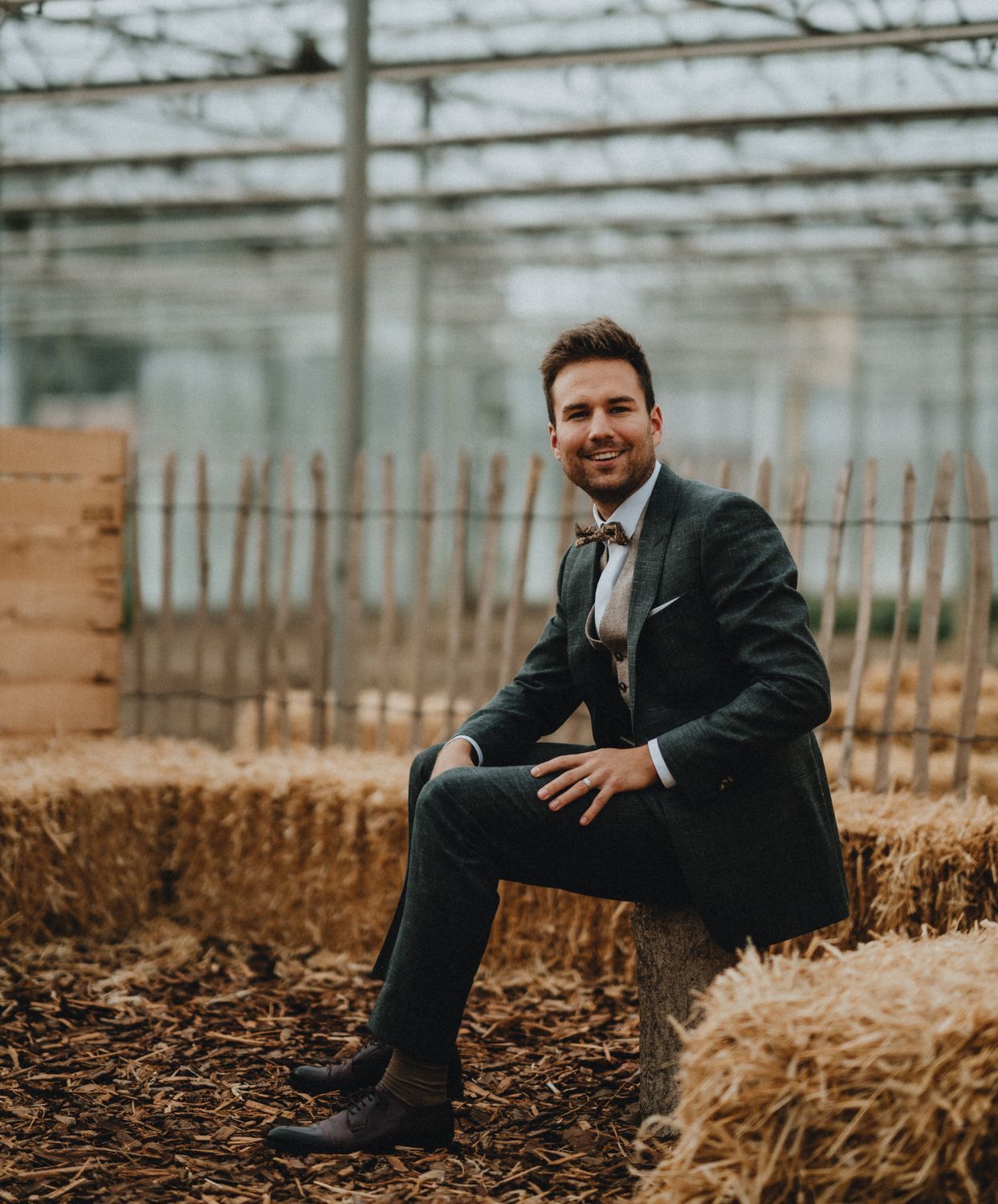 Artistic wedding photography series featuring groom poses near rustic greenhouse.