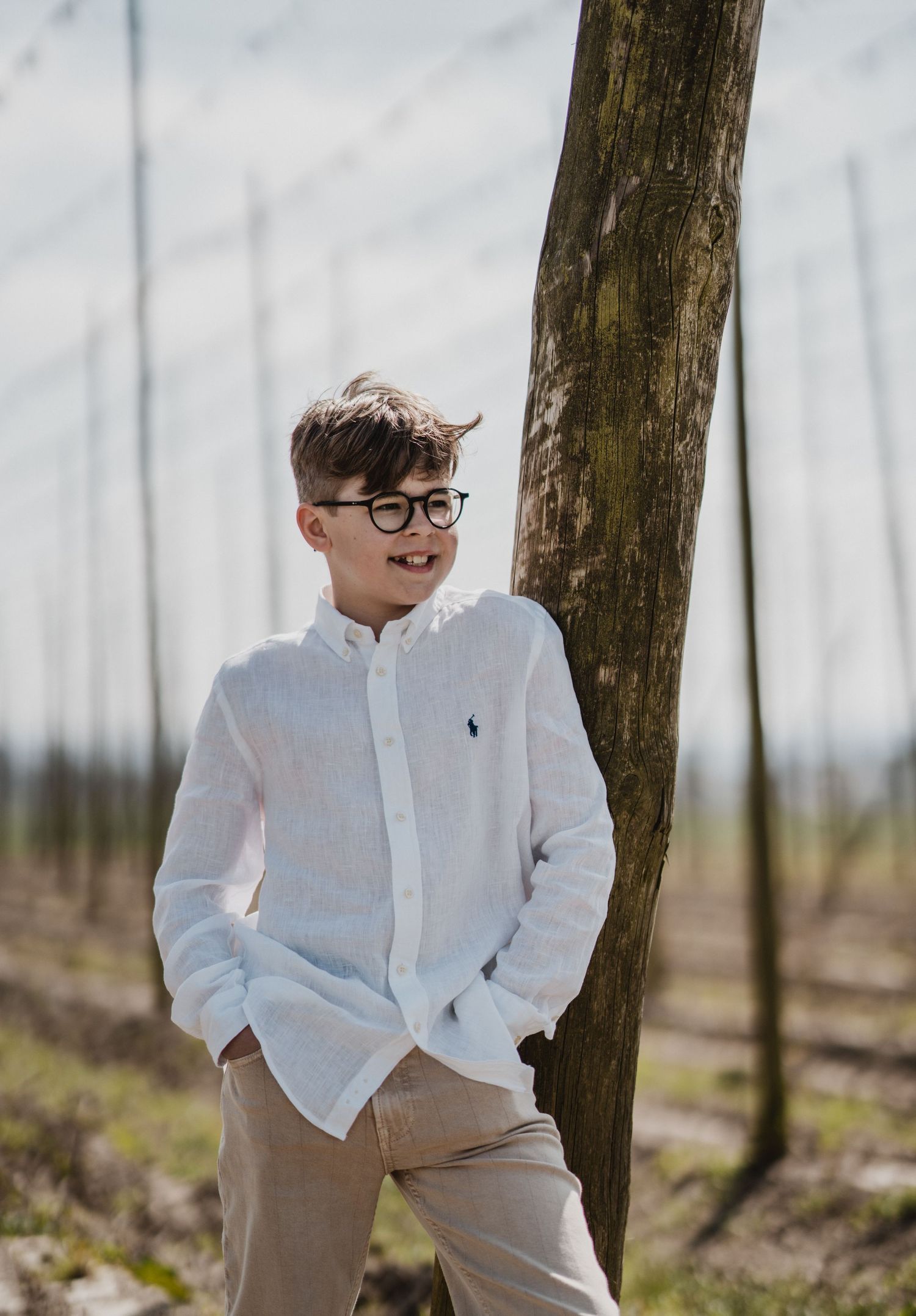 A bright outdoor portrait near wooden posts wearing a crisp white shirt.