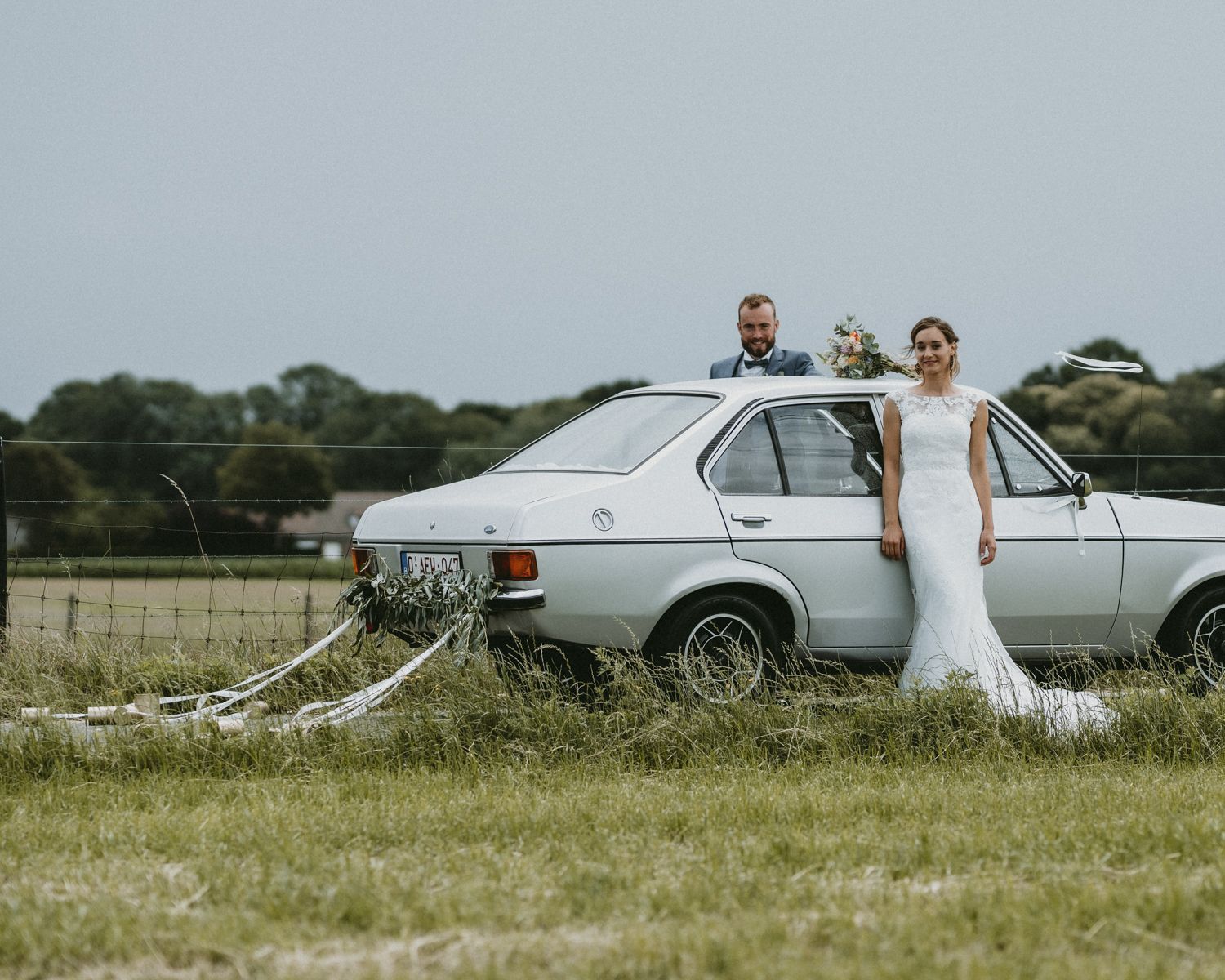 Wedding scene with classic cars parked in a sunny field.