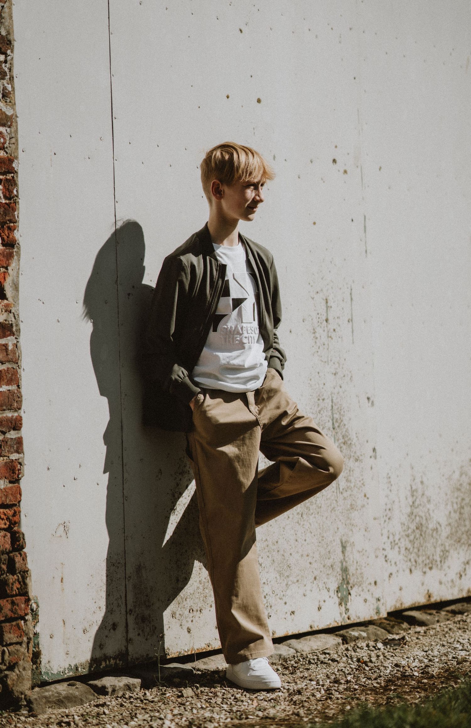 Someone poses against a white wall wearing casual clothing and sneakers.