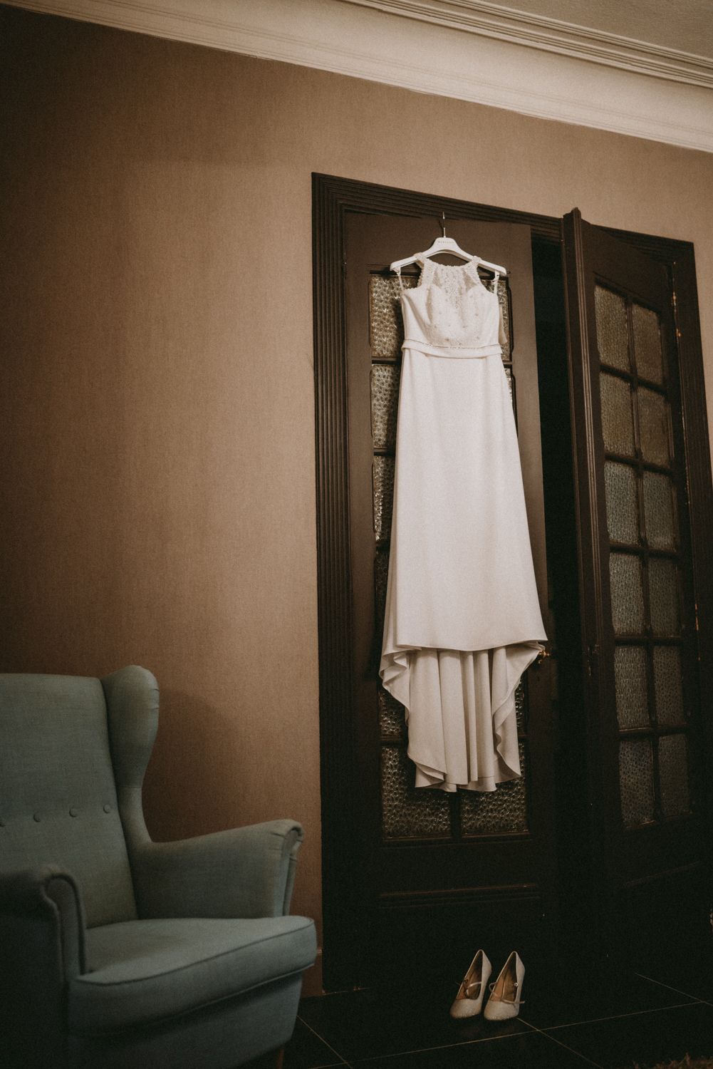 White wedding dress hanging elegantly against dark wooden doors with shoes below.