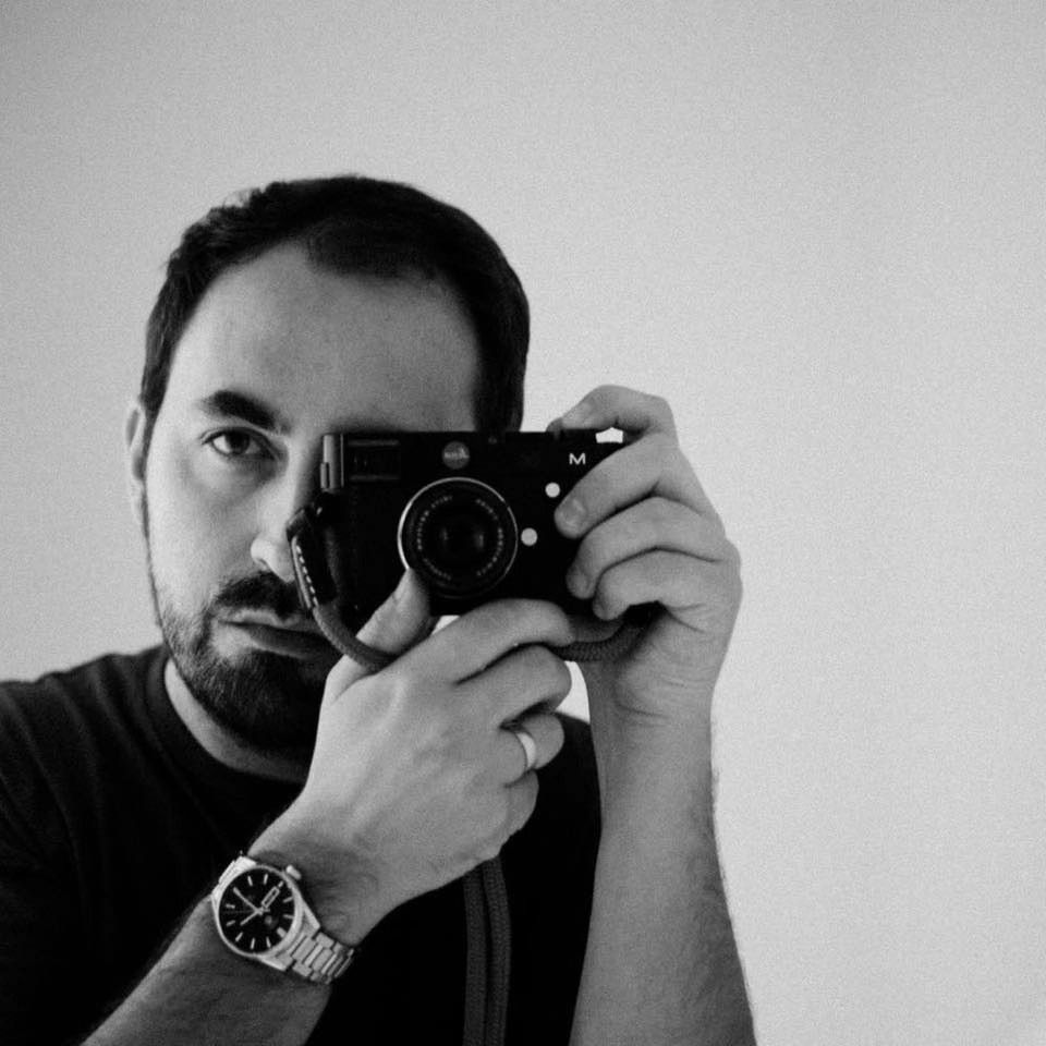 Photographer taking self portraits in black and white against plain backdrop.