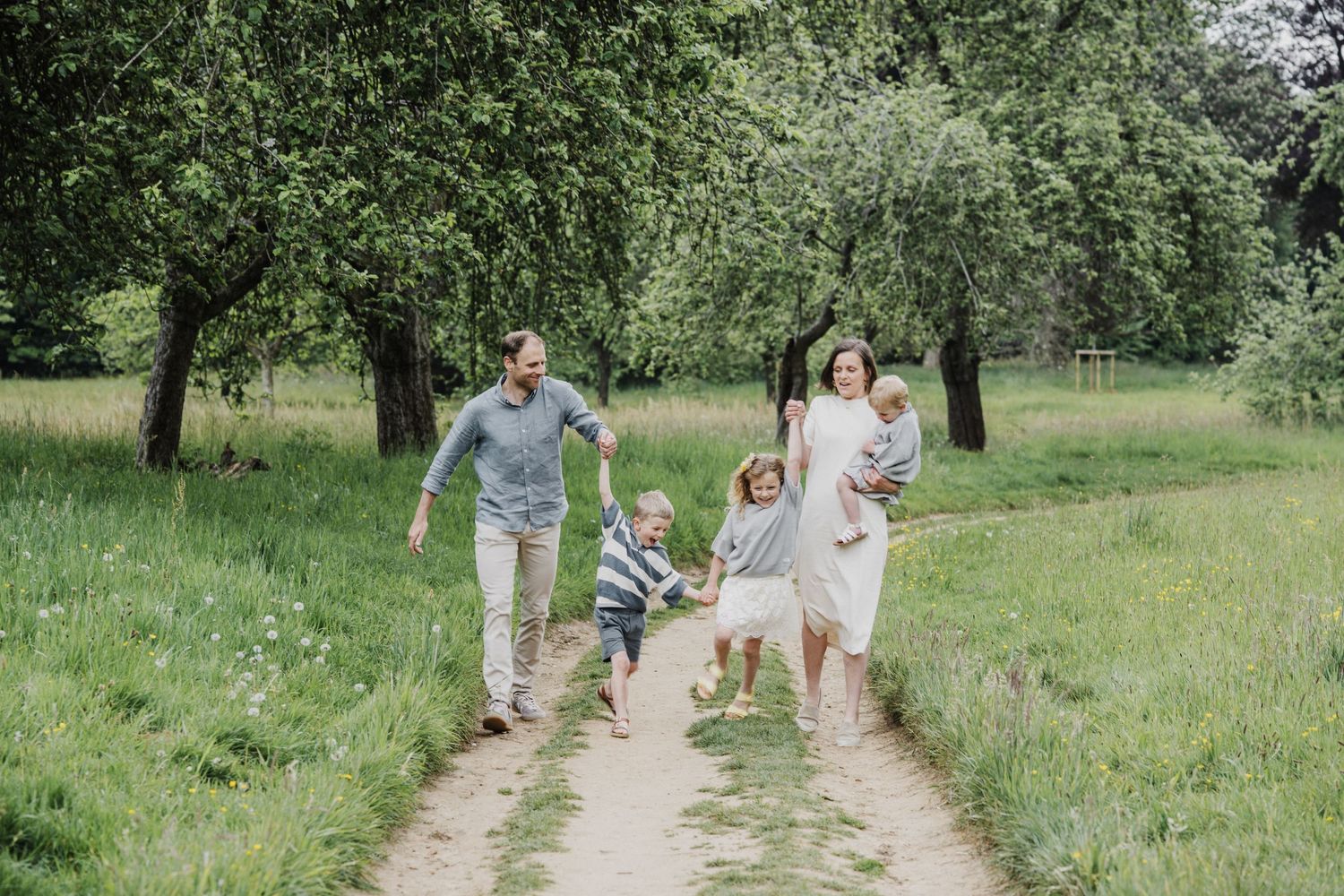 Happy family with young children walking together on a sunny path through a lush green park.