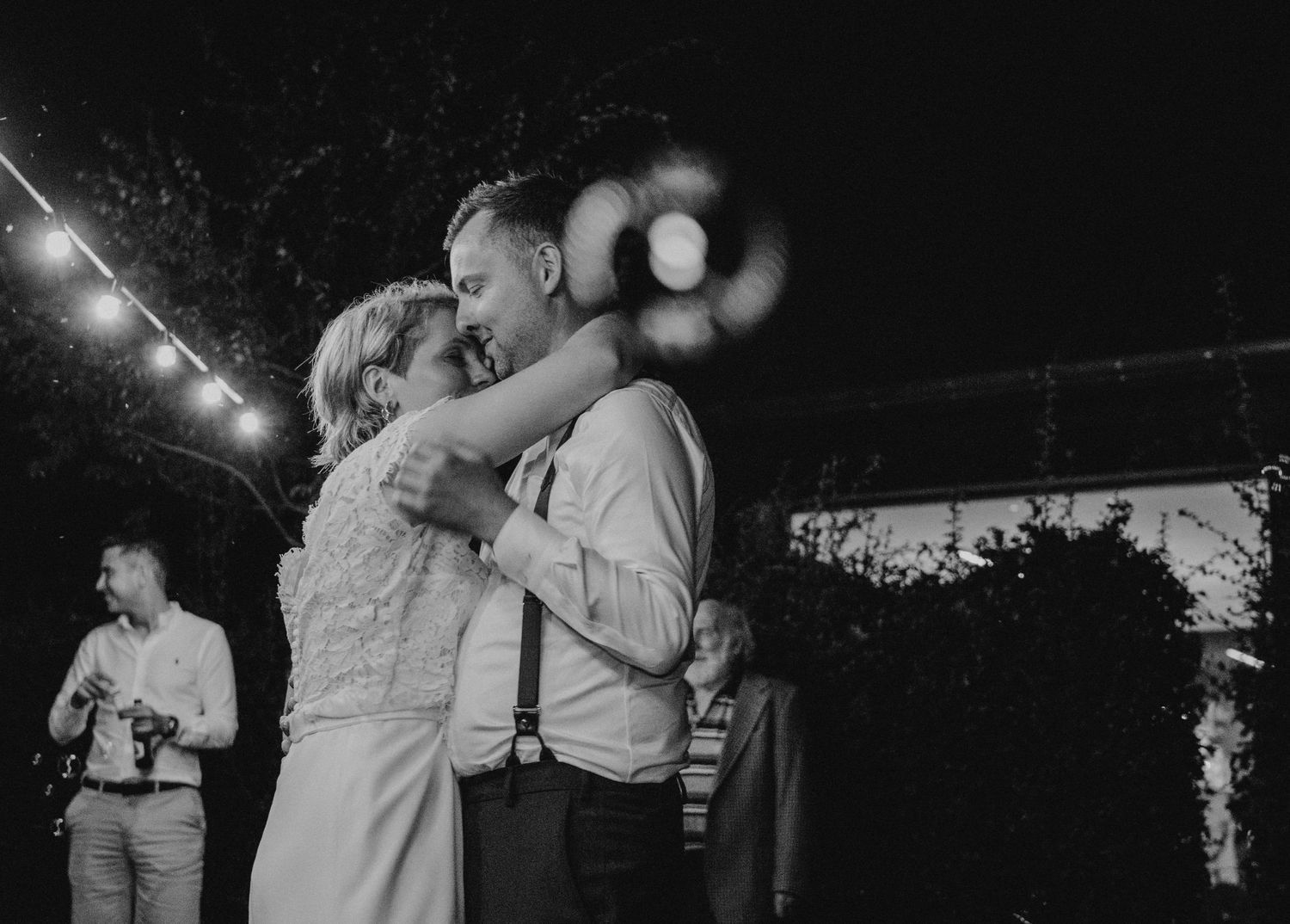 A romantic evening dance moment under twinkling lights at an outdoor wedding reception.