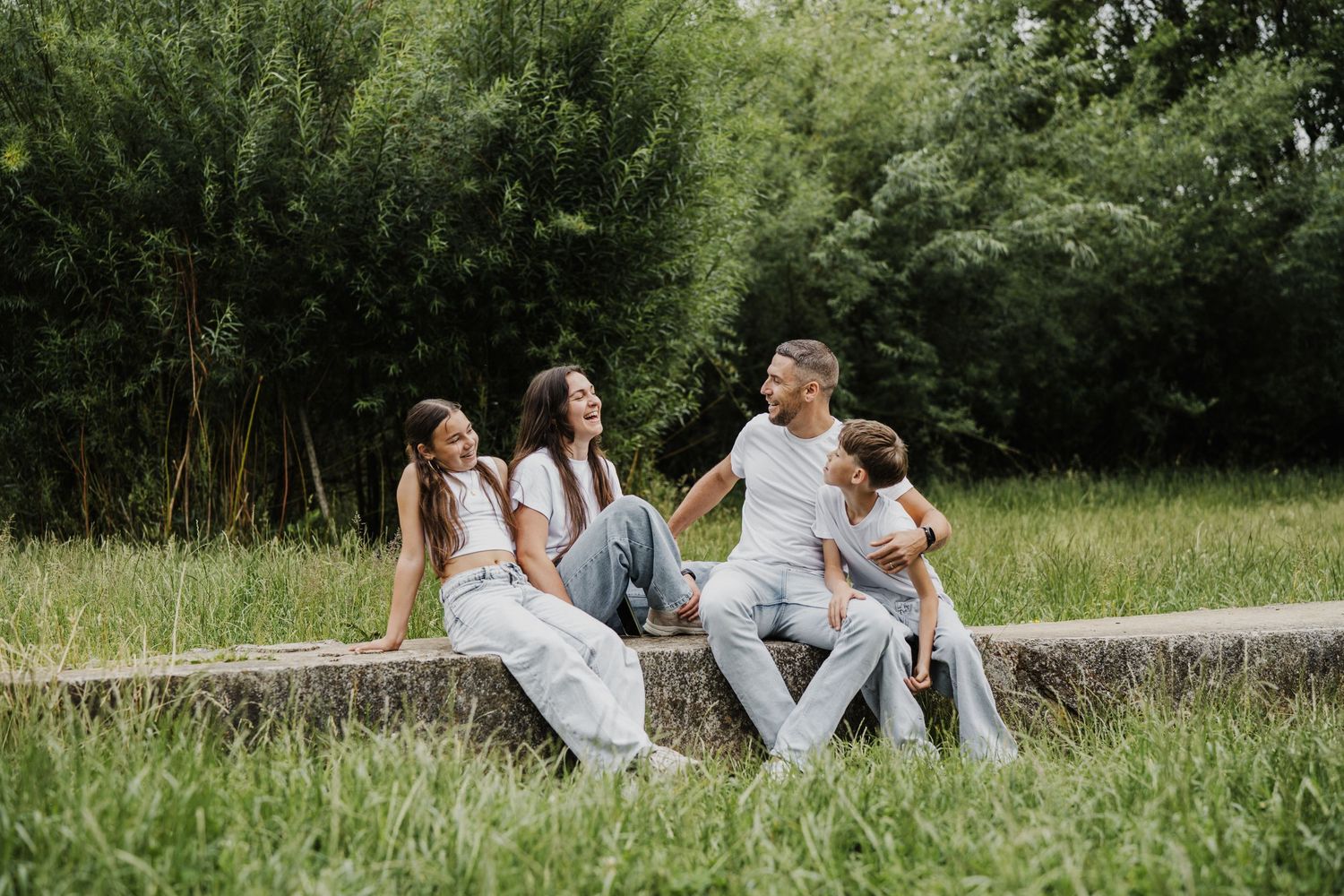 A group sits together on a stone wall surrounded by lush greenery on a sunny summer day.