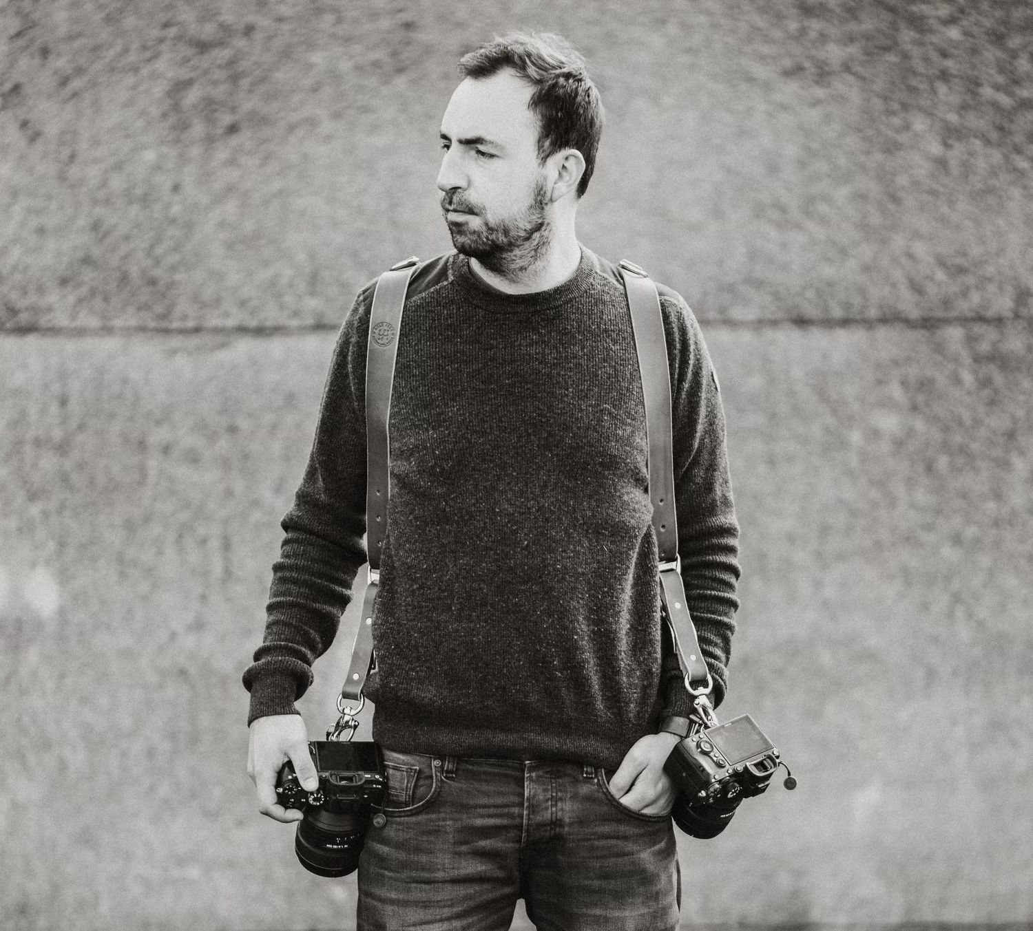 Black and white sequence showing a photographer holding dual cameras against a gray wall.