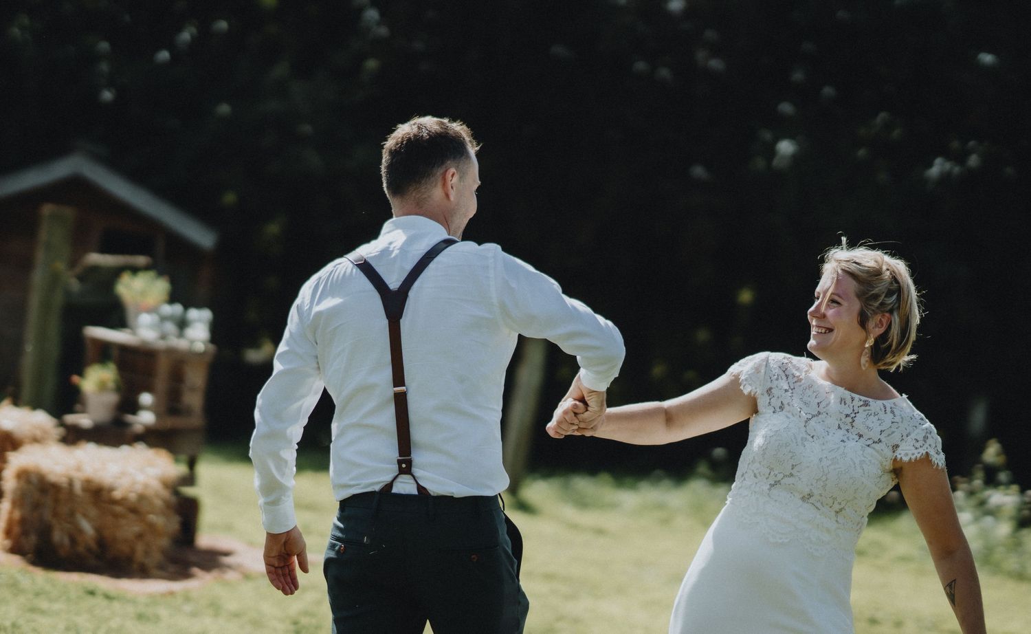 A playful wedding moment in a sunny garden with hay bales in the background.