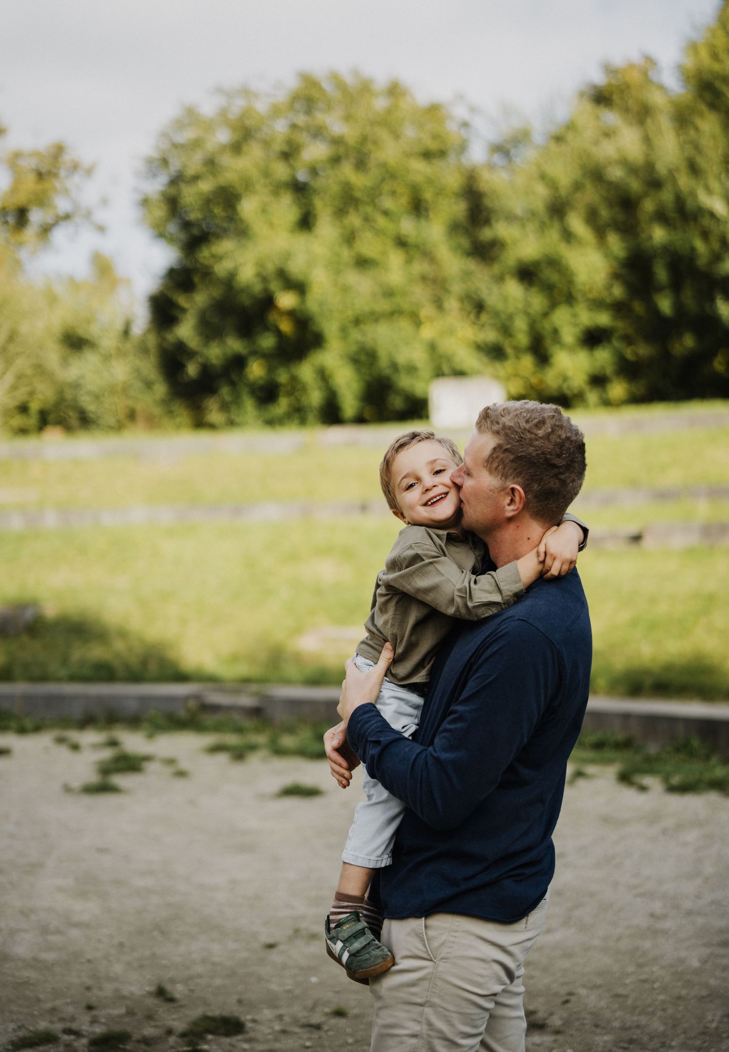 A parent and child share a tender moment together on a beach with trees in the background.