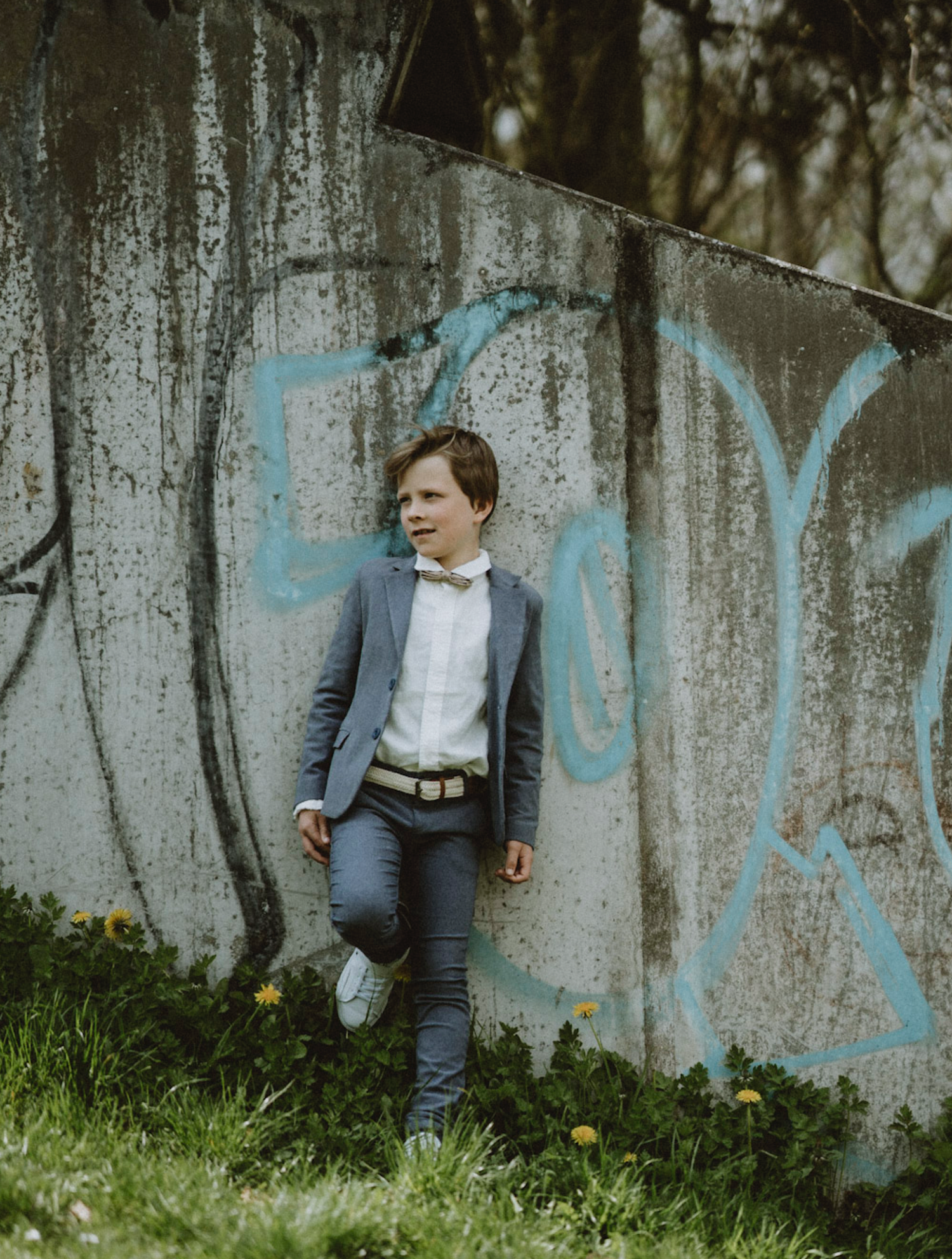 A casual portrait against a graffiti wall features someone in a grey blazer and white shirt.