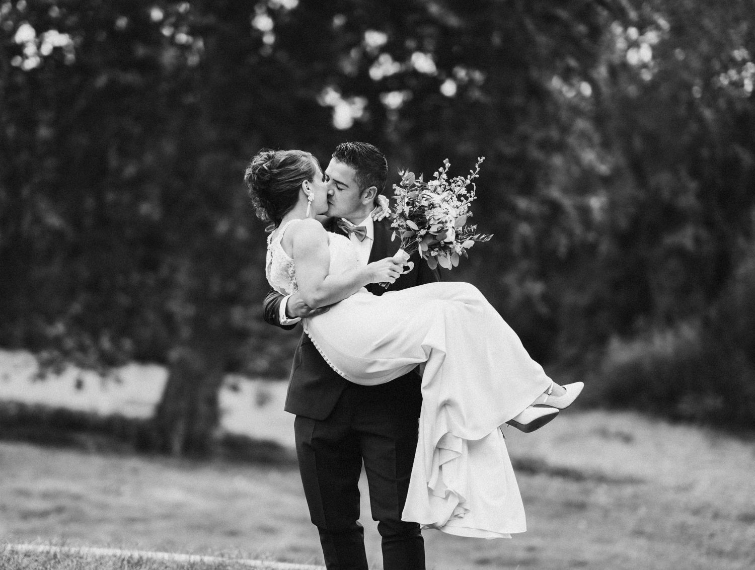 Black and white wedding photo of a joyful lift pose in a garden setting.