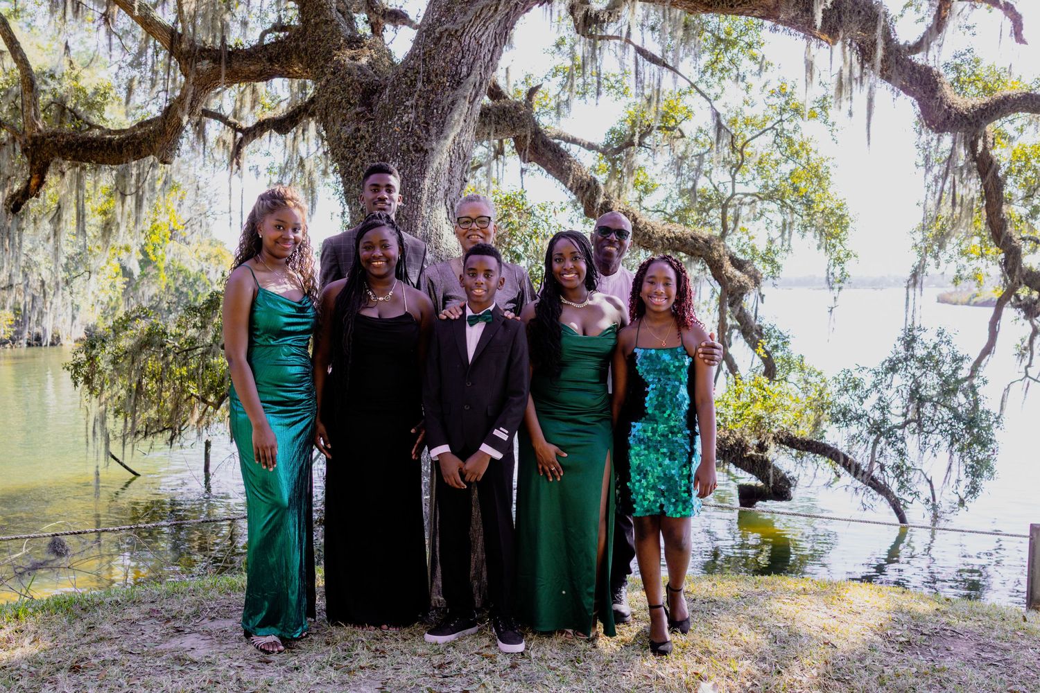 Wedding party poses together under Spanish moss draped trees in emerald green and black formal attire.