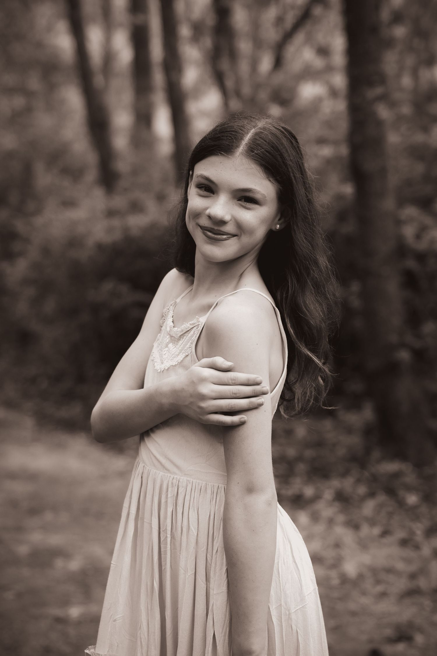 Black and white portrait of someone in a flowing white dress against a wooded background.