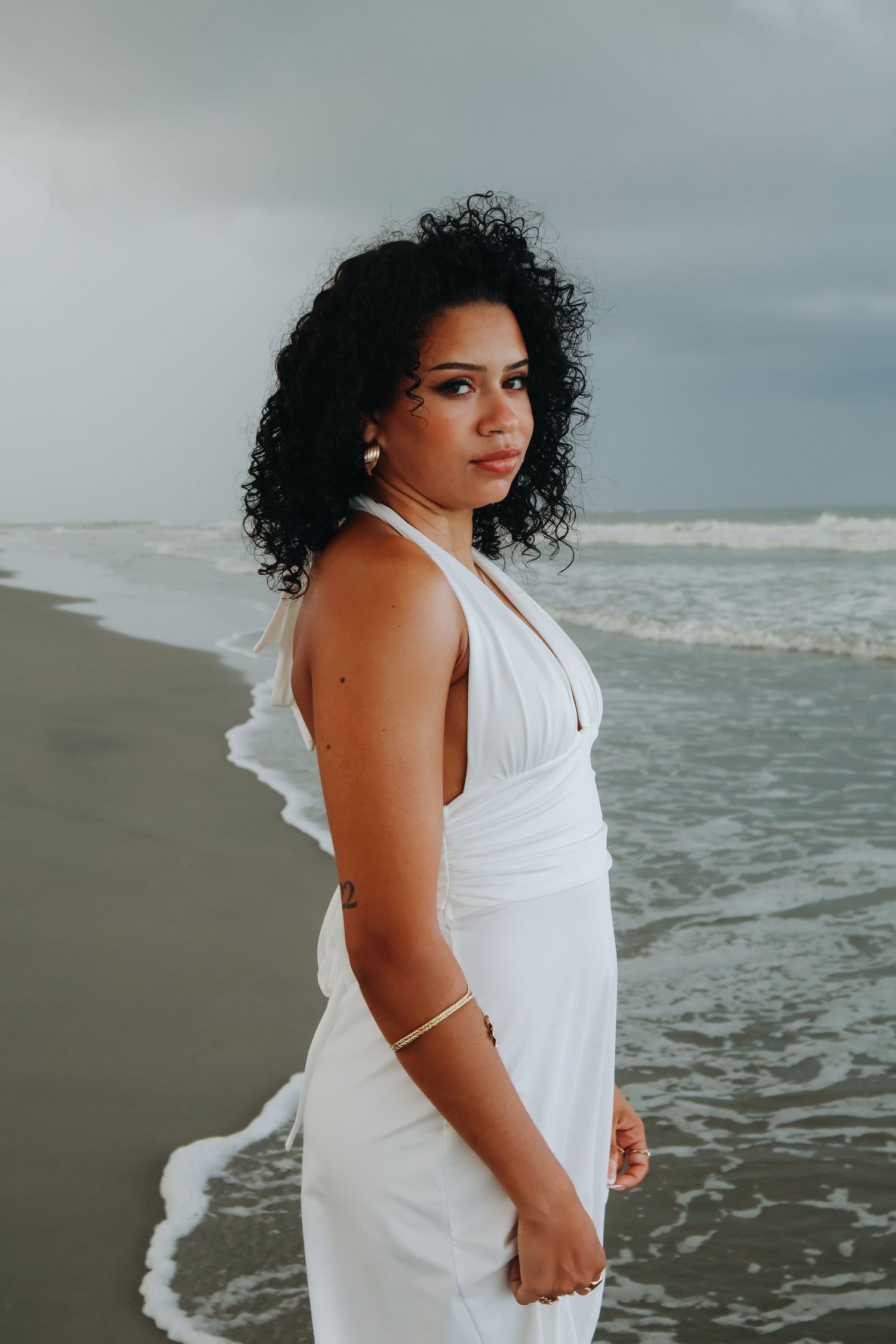 Elegant beach photoshoot with waves and cloudy sky in the background.