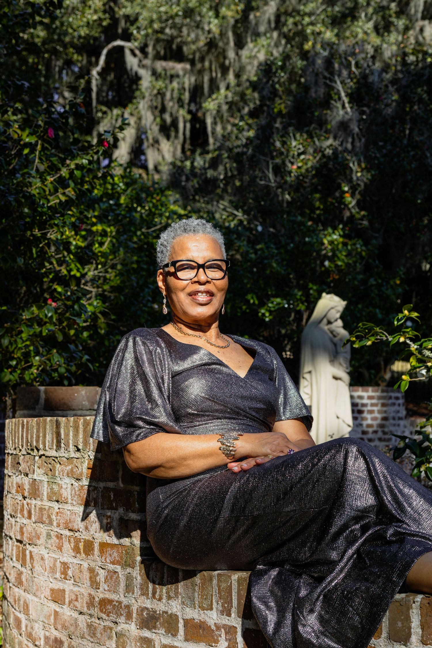 Person in a sparkly black dress reclines on brick wall outdoors.