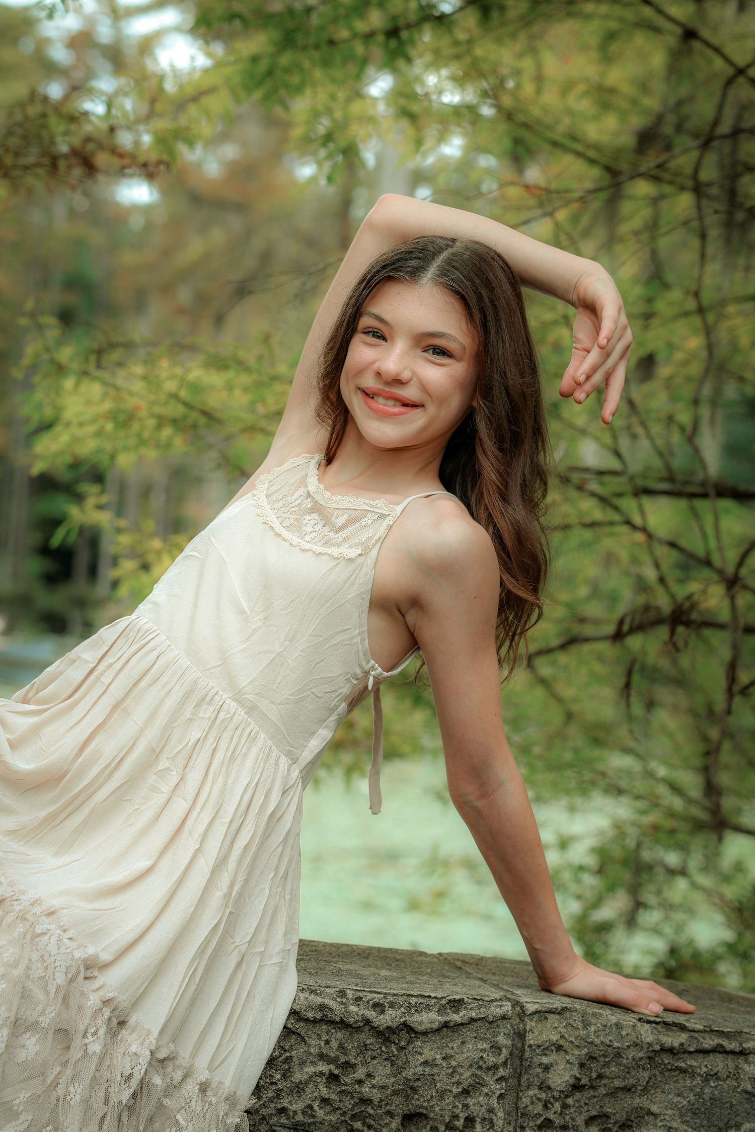 A dancer poses gracefully on a stone wall in a cream-colored vintage dress.