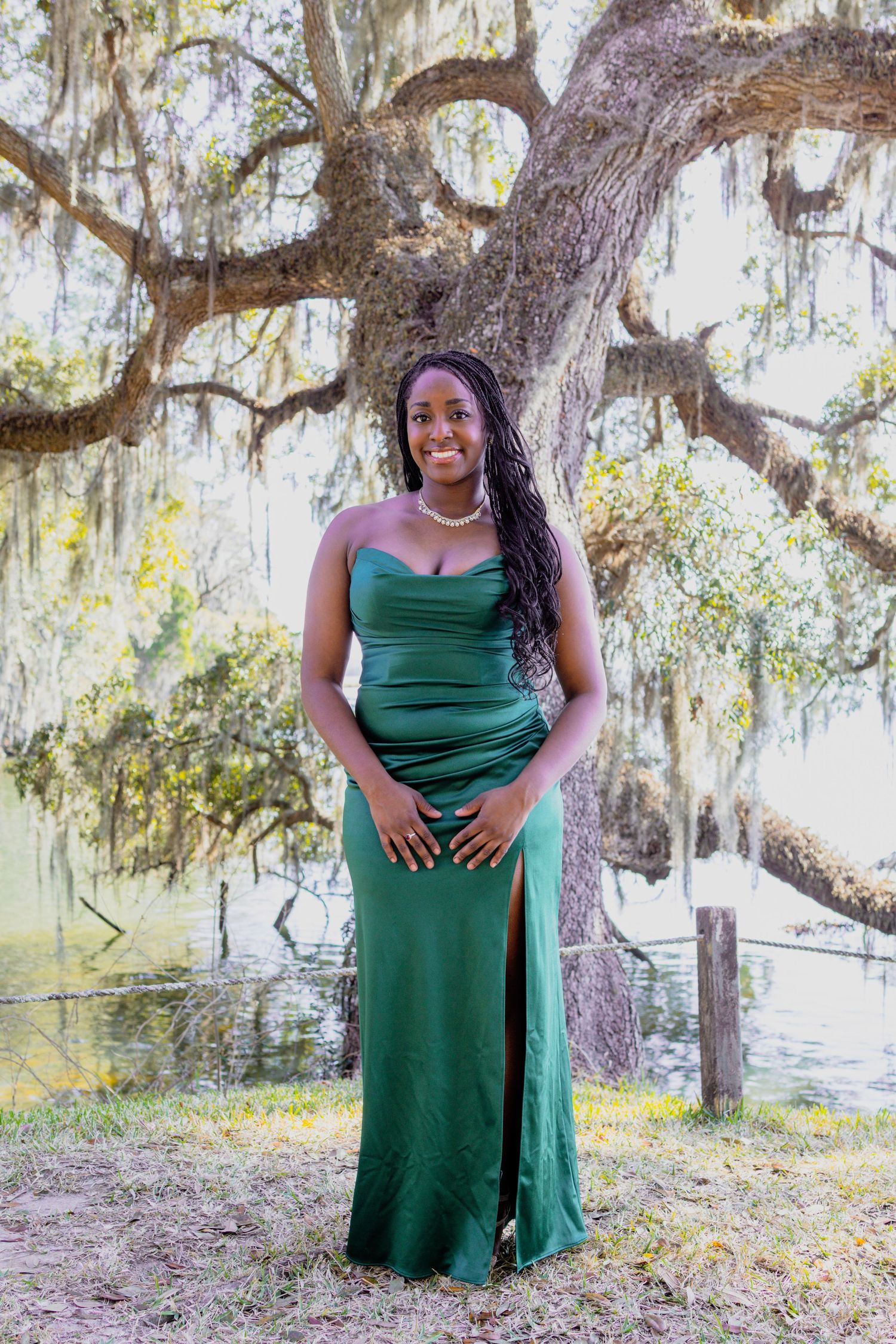 Person in flowing green dress stands gracefully under oak trees with Spanish moss.