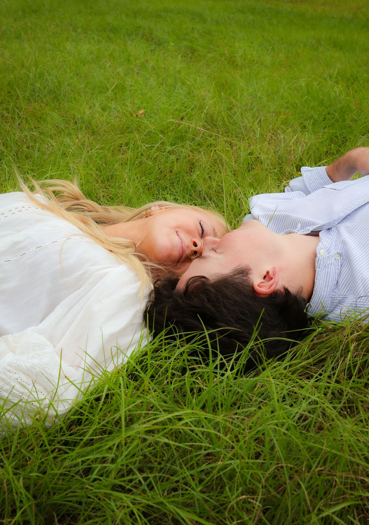 A couple lying in tall green grass during a romantic photoshoot.