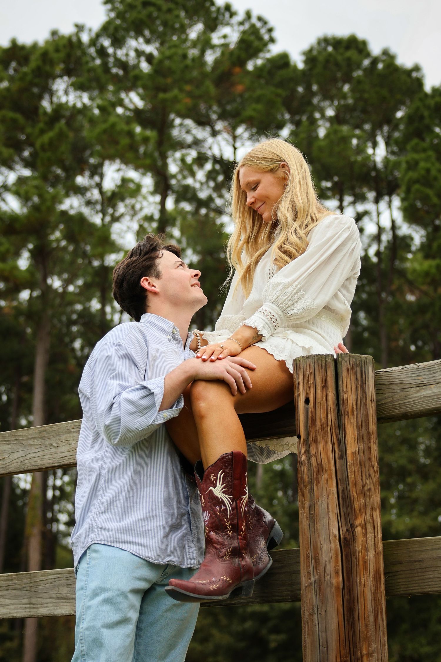 A playful scene of two people interacting by a wooden fence wearing boots.