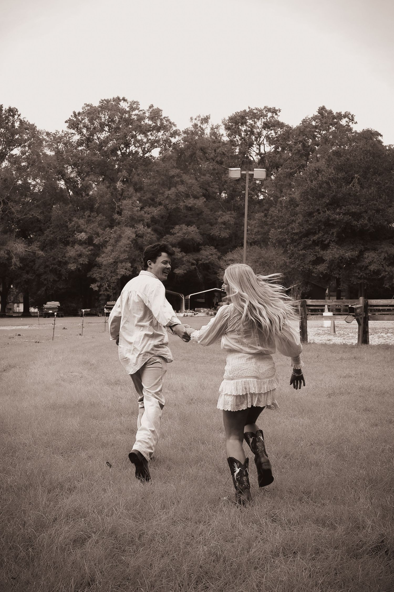 Two people running playfully through an open field at dusk.