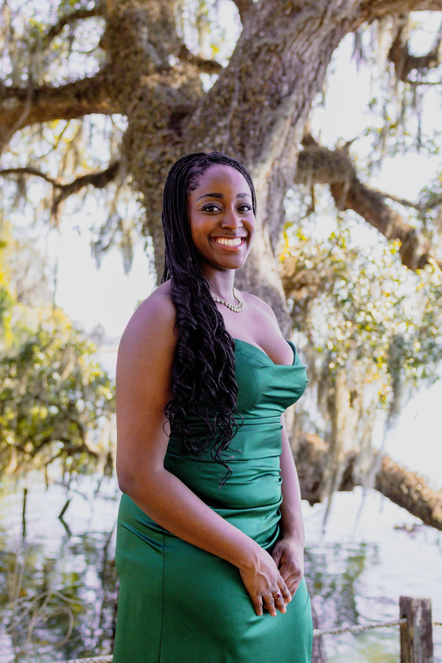 Person in emerald green dress poses elegantly under Spanish moss draped trees.