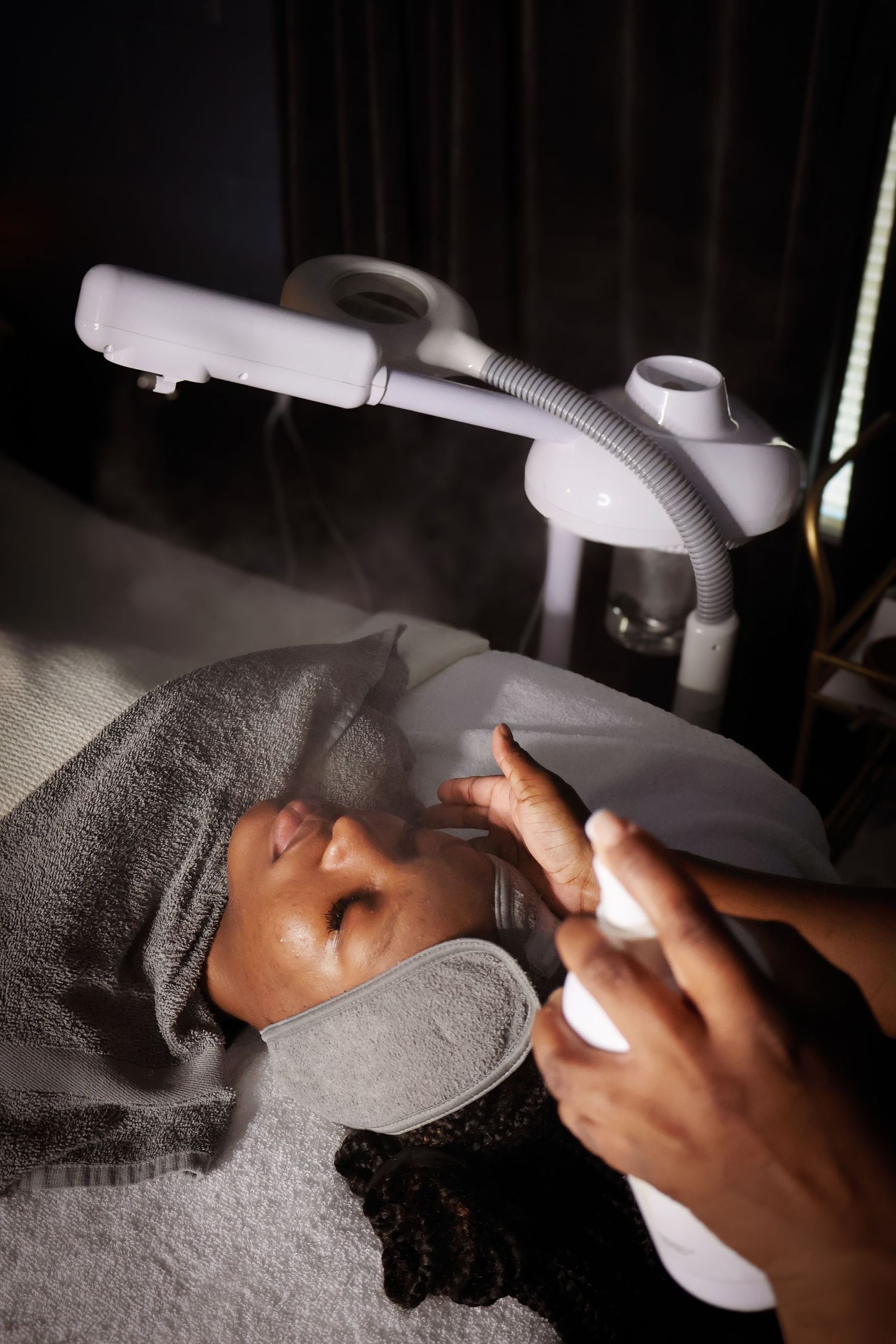 Close-up of hands applying facial treatment products in a dark spa environment.
