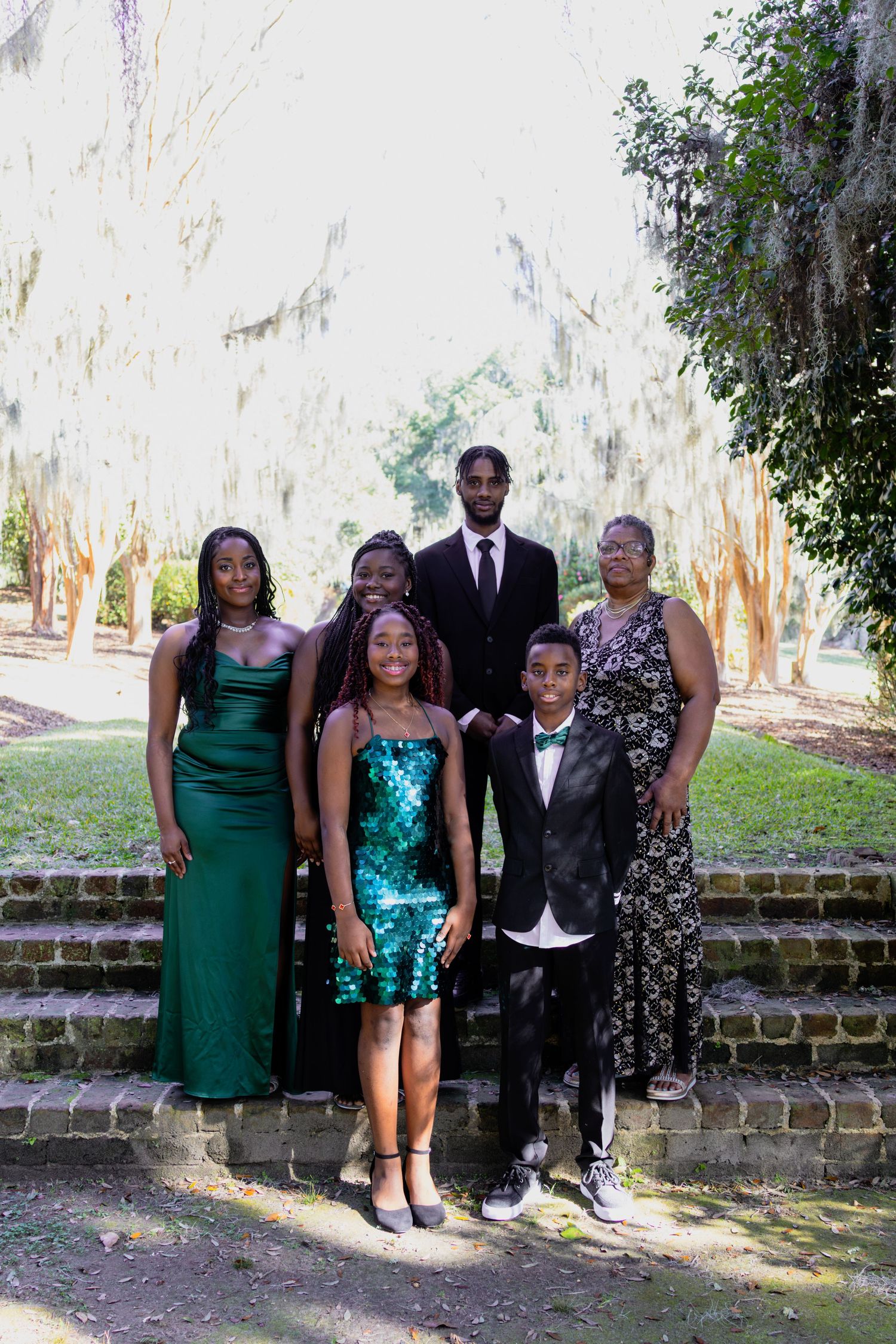Formal group portrait against a brick wall with people wearing elegant attire in green and black.