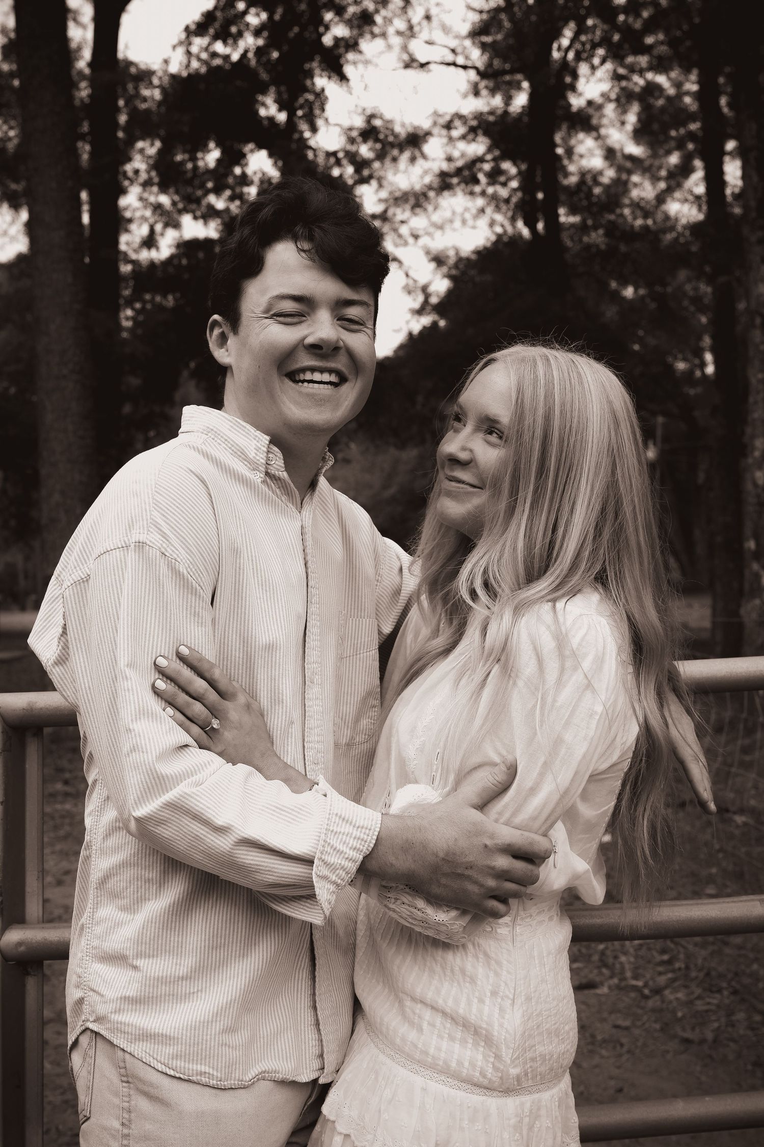 A couple in matching white outfits shares joyful laughter during an outdoor photoshoot.