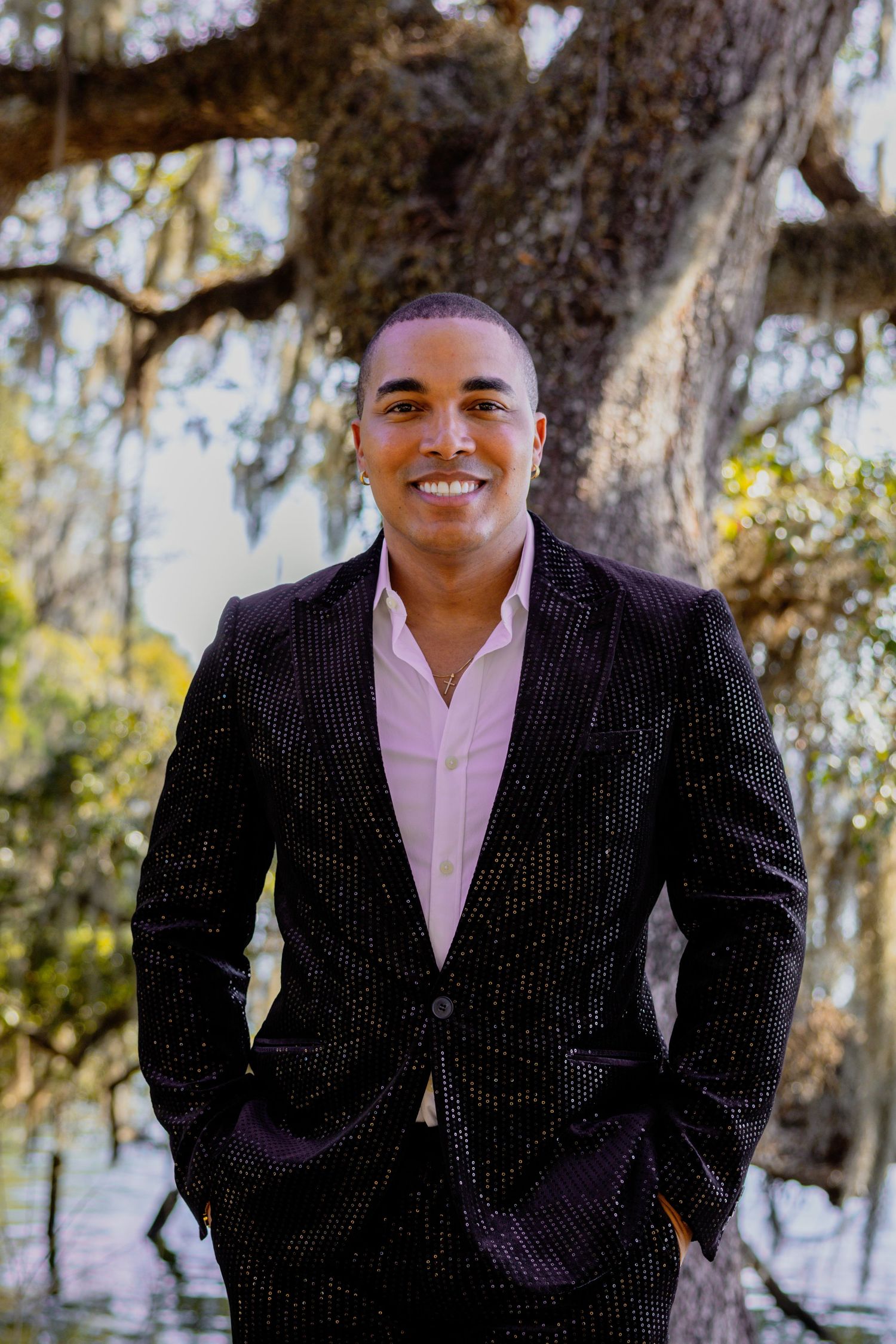 Person in dark suit and pink shirt poses confidently outdoors.