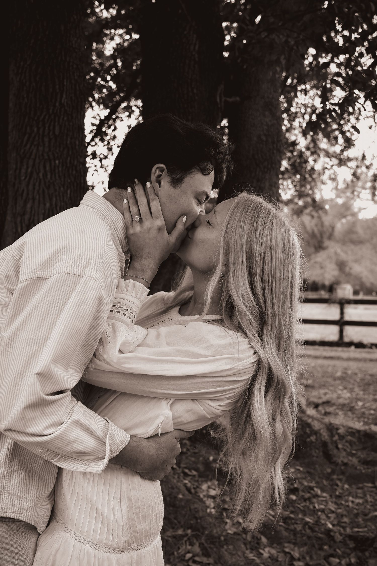 A romantic couple in white clothing sharing intimate moments under a large tree.