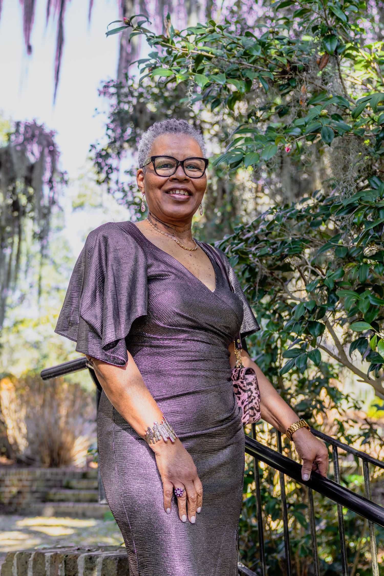 Person in a purple dress poses outdoors against a backdrop of lush greenery and Spanish moss.