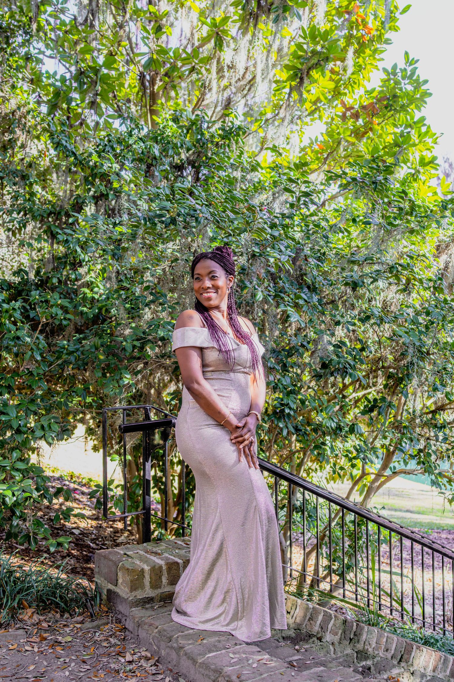 Person in a blush pink dress poses gracefully on stone steps surrounded by greenery.