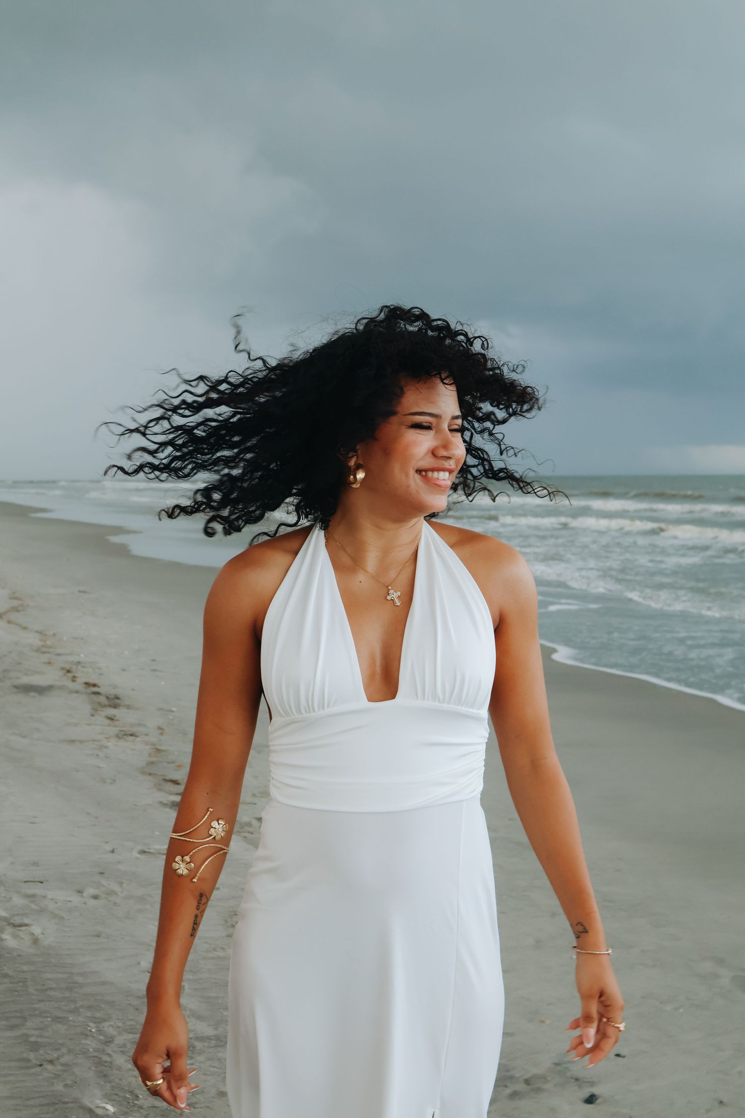 Person in flowing white dress twirling joyfully on a windy beach.