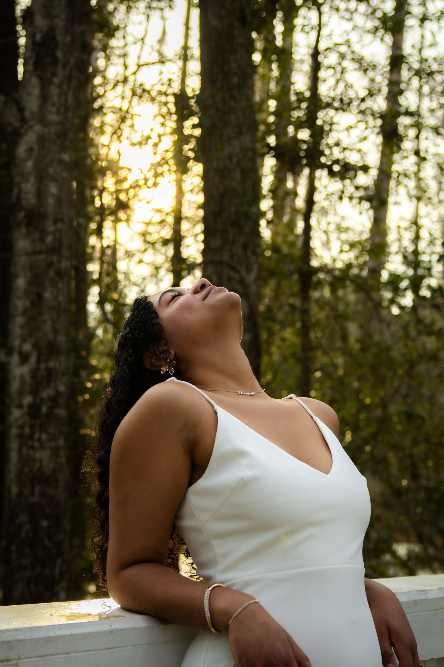 Artistic portrait in a forest setting with golden sunlight filtering through pine trees.