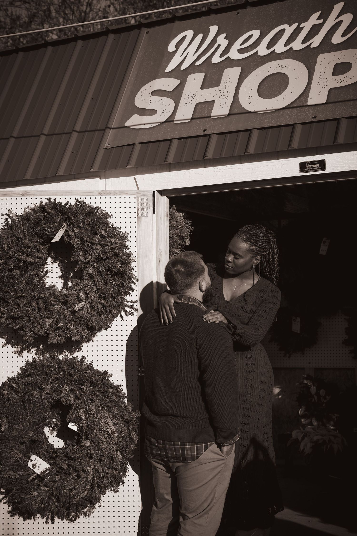 Holiday shoppers browse wreaths at rustic Christmas shop exterior.