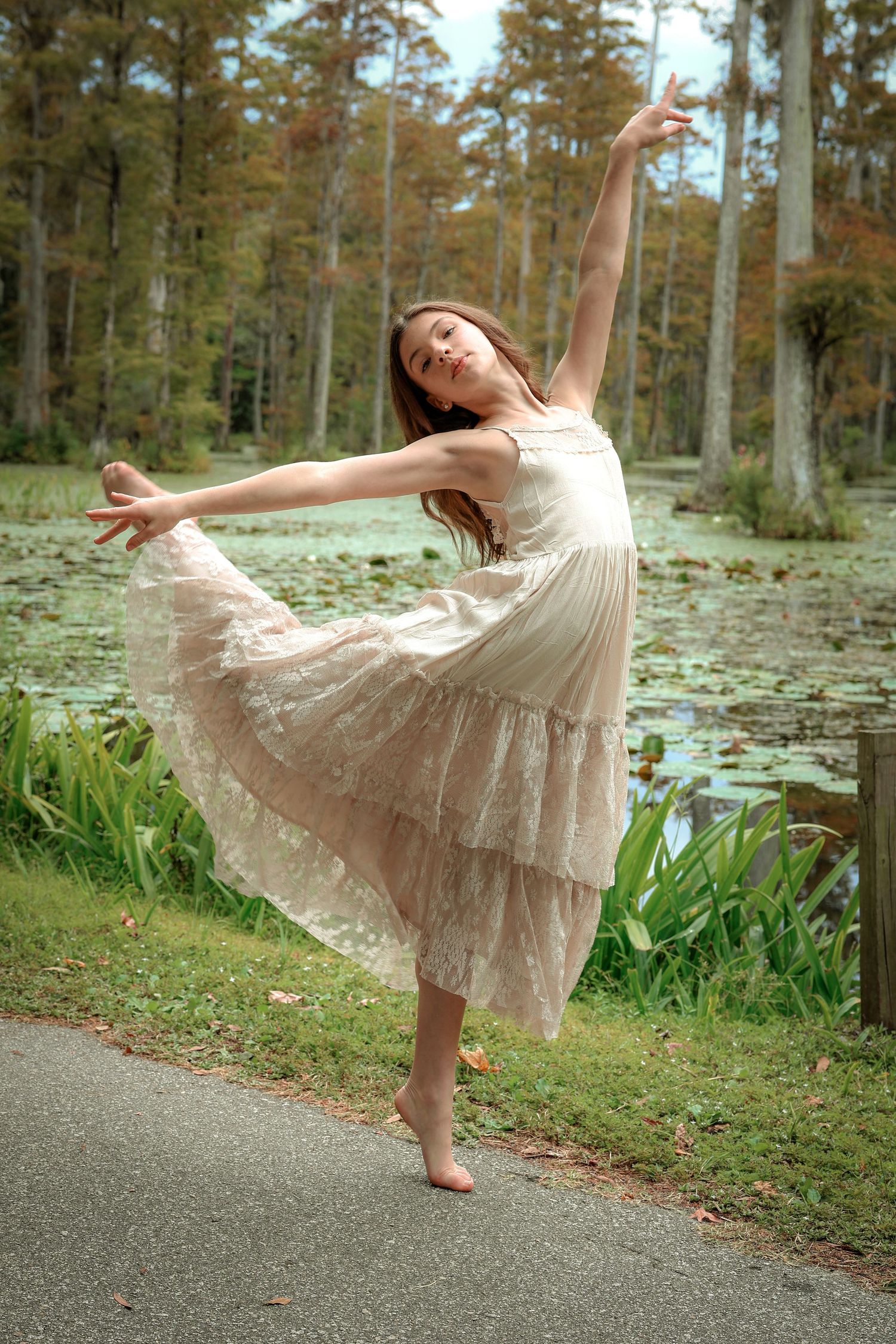A dancer in a flowing cream dress performs an elegant pose in a forest setting.