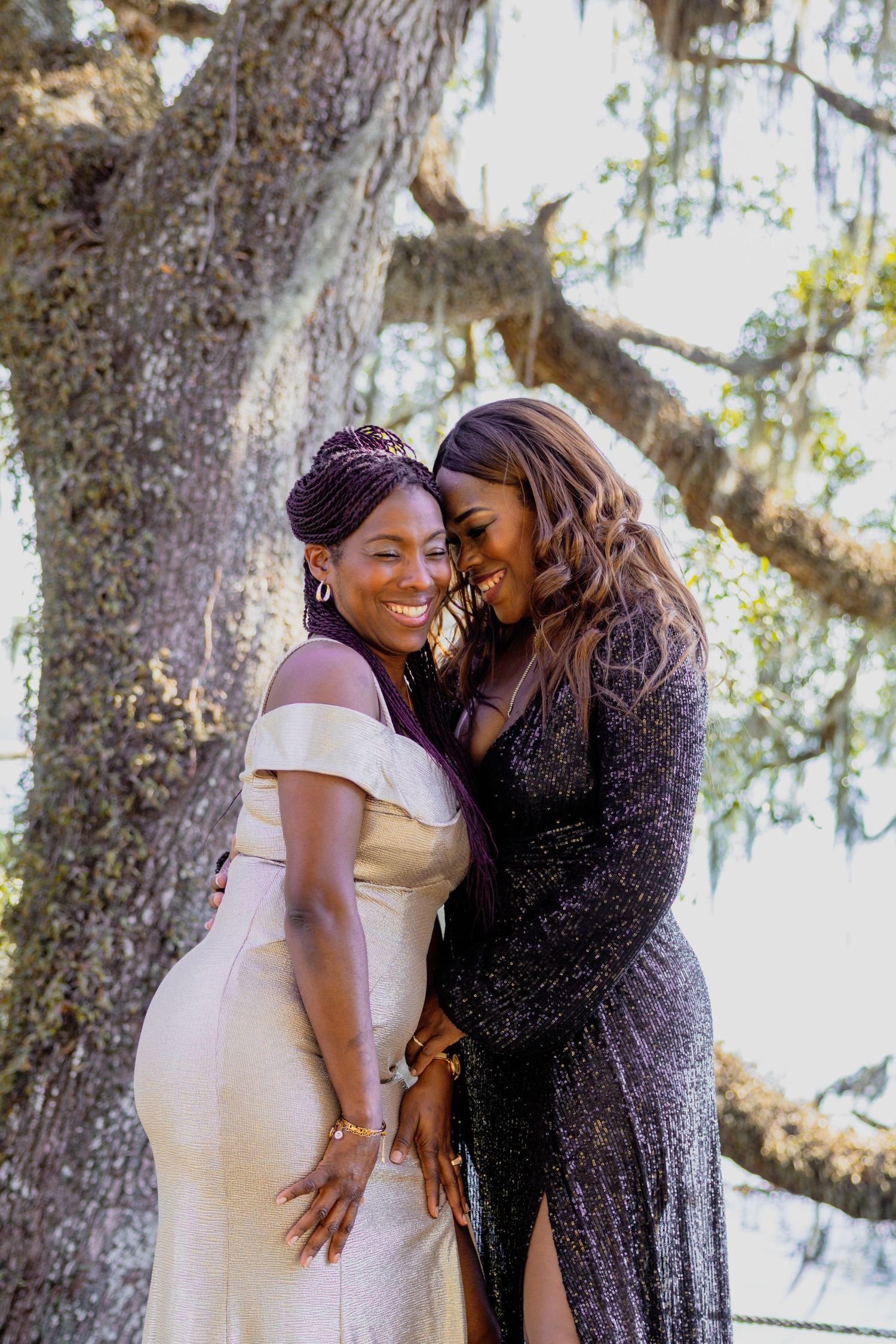 Two people in formal attire sharing an intimate moment under a tree with Spanish moss.