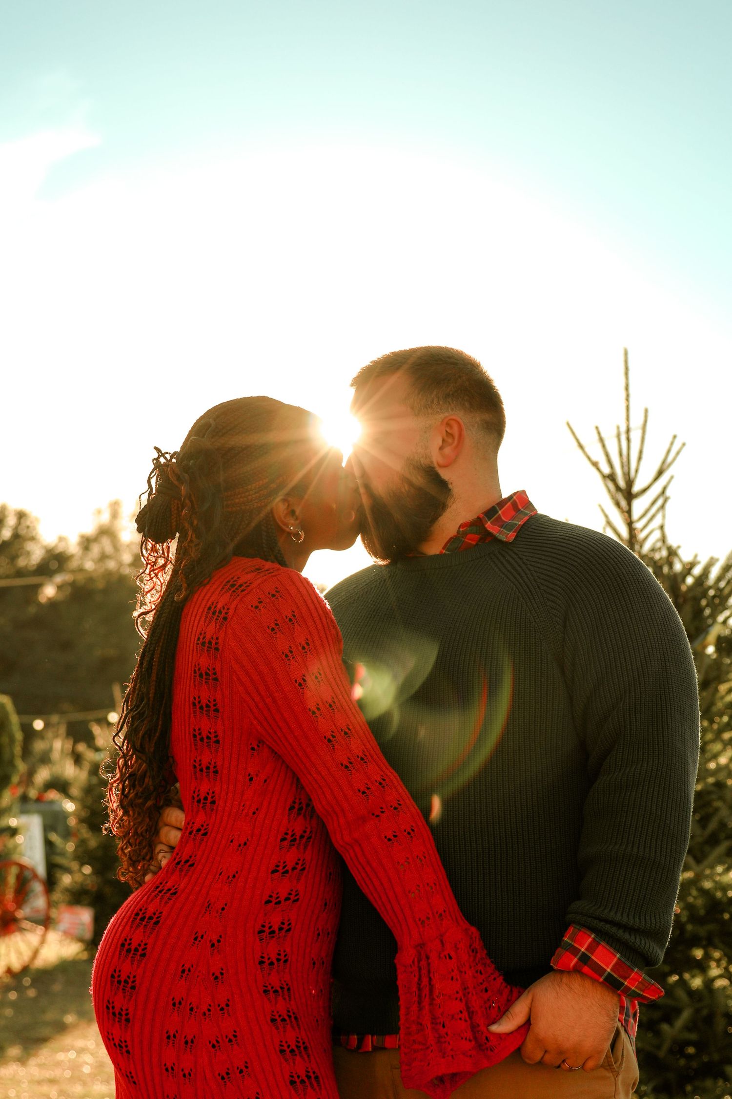 Silhouetted couple embracing at Christmas tree farm during golden hour sunset.