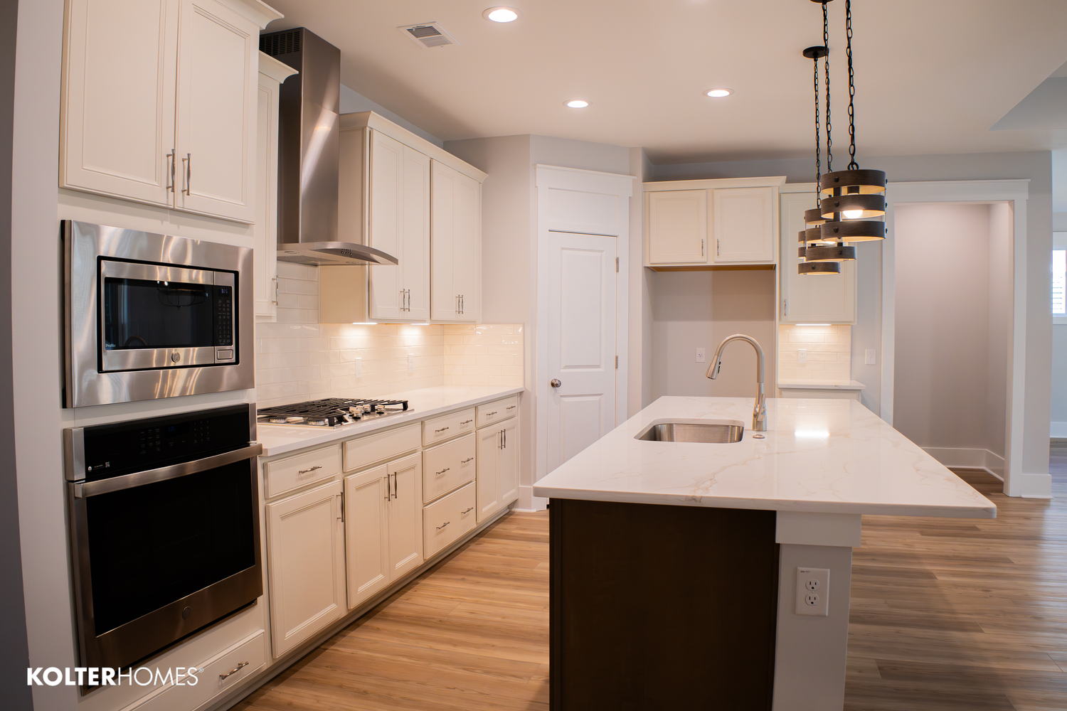 Modern white kitchen with quartz countertops, stainless appliances and pendant lighting.
